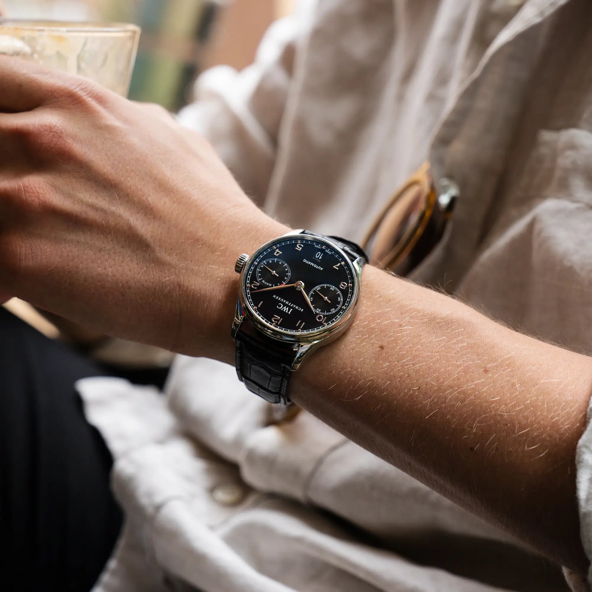 Mann trägt die Portugieser 7 Days Automatic IW500109 Uhr von IWC Schaffhausen am schwarzen Lederband mit schwarzem Zifferblatt an seinem Handgelenk