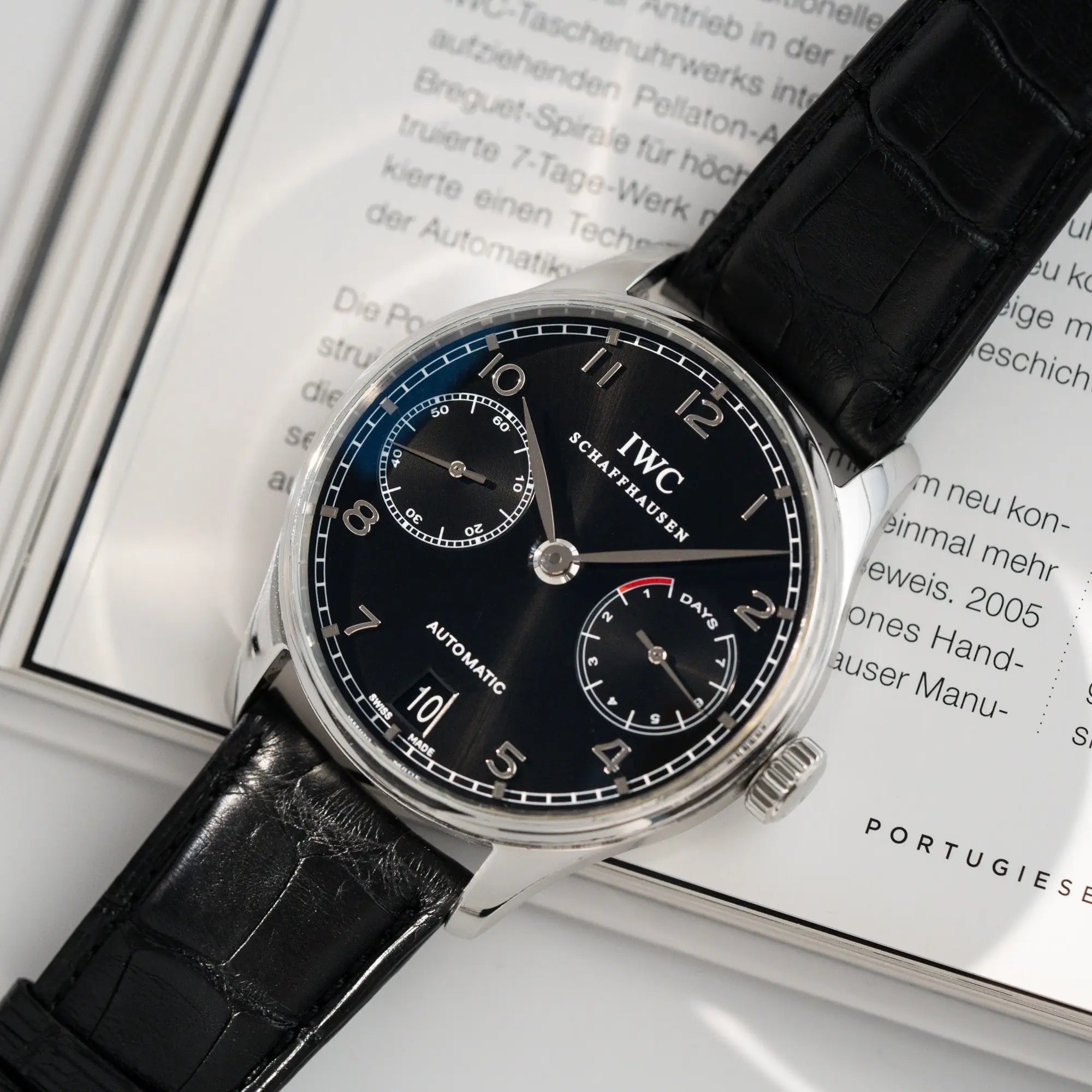 Detailaufnahme der Portugieser 7 Days Automatic IW500109 Uhr von IWC Schaffhausen am schwarzen Lederband mit Fokus auf dem schwarzen Zifferblatt und dem Edelstahl-Gehäuse