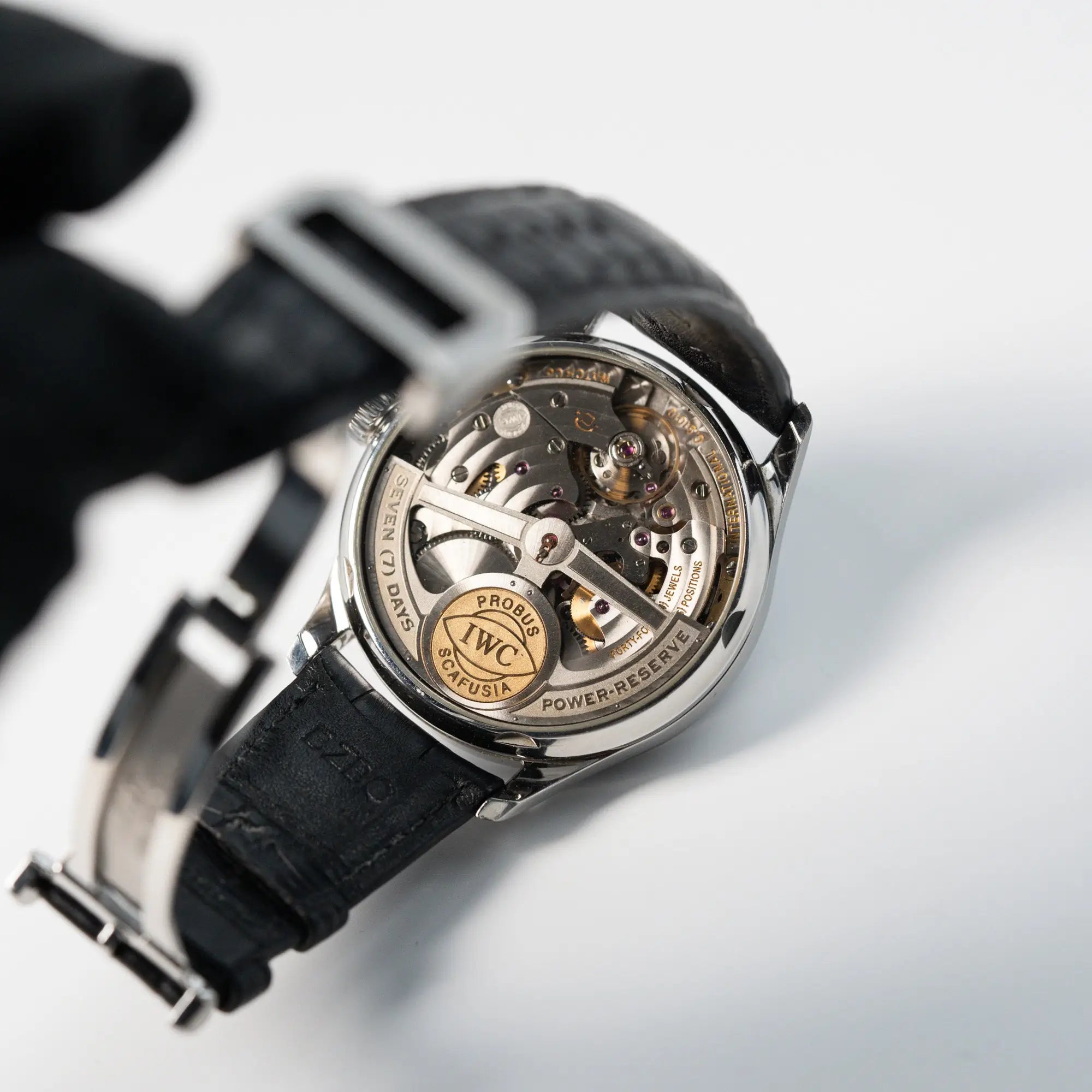 Produktfotografie der Portugieser 7 Days Automatic IW500109 Uhr von IWC Schaffhausen am schwarzen Lederband mit Blick auf das Uhrwerk durch den Gehäuseboden aus Glas