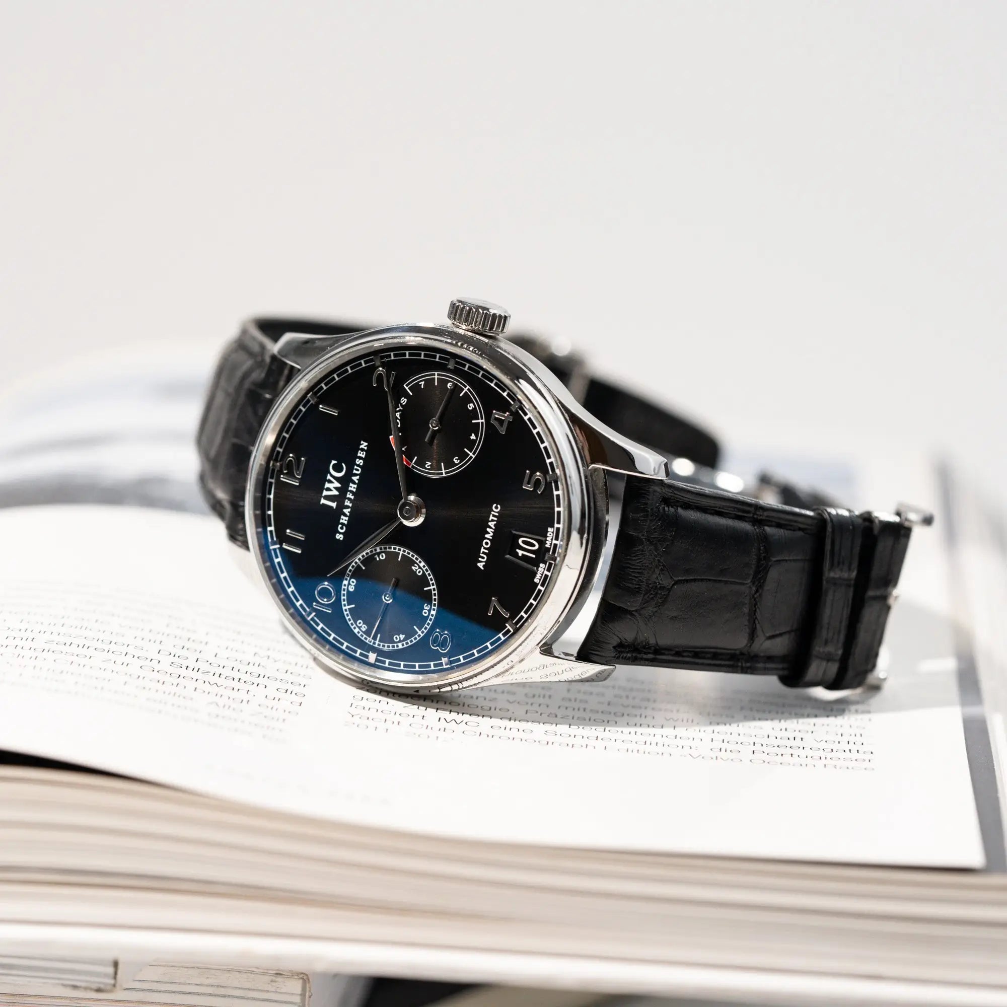 Produktfotografie der seitlich liegenden Portugieser 7 Days Automatic IW500109 Uhr von IWC Schaffhausen am schwarzen Lederband mit schwarzem Zifferblatt