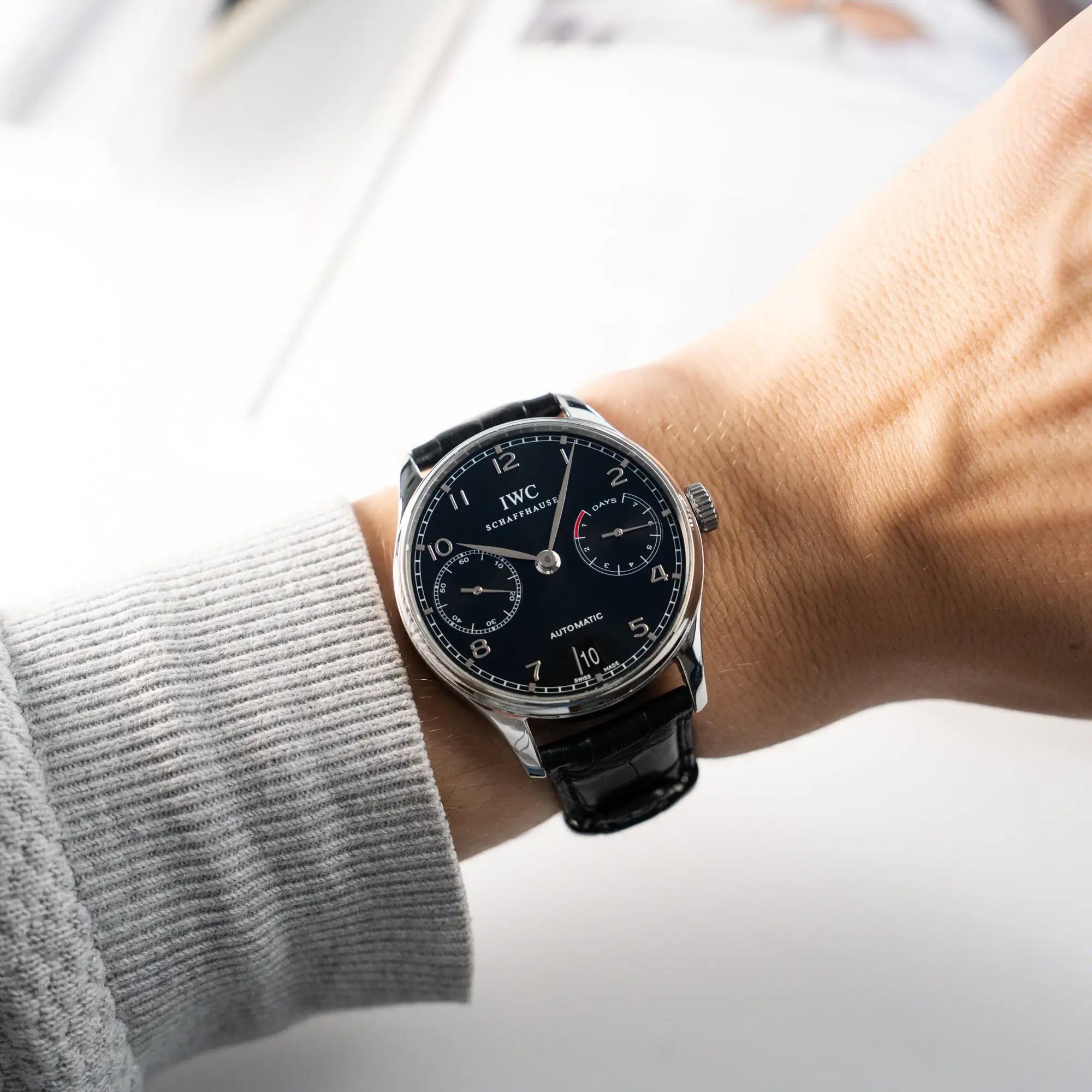 Wristshot mit der Portugieser 7 Days Automatic IW500109 Uhr von IWC Schaffhausen am schwarzen Lederband mit Fokus auf dem schwarzen Zifferblatt und dem Edelstahl-Gehäuse