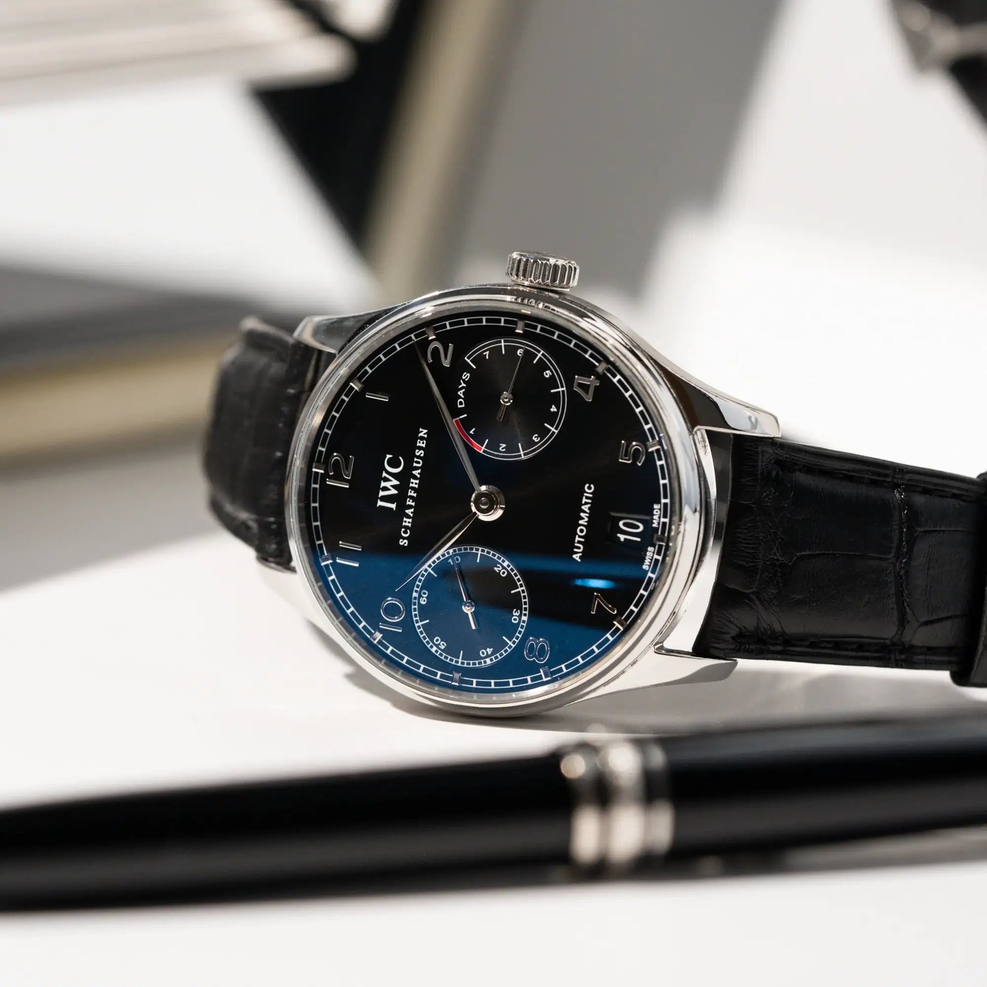 Produktfotografie der seitlich liegenden Portugieser 7 Days Automatic IW500109 Uhr von IWC Schaffhausen am schwarzen Lederband mit schwarzem Zifferblatt