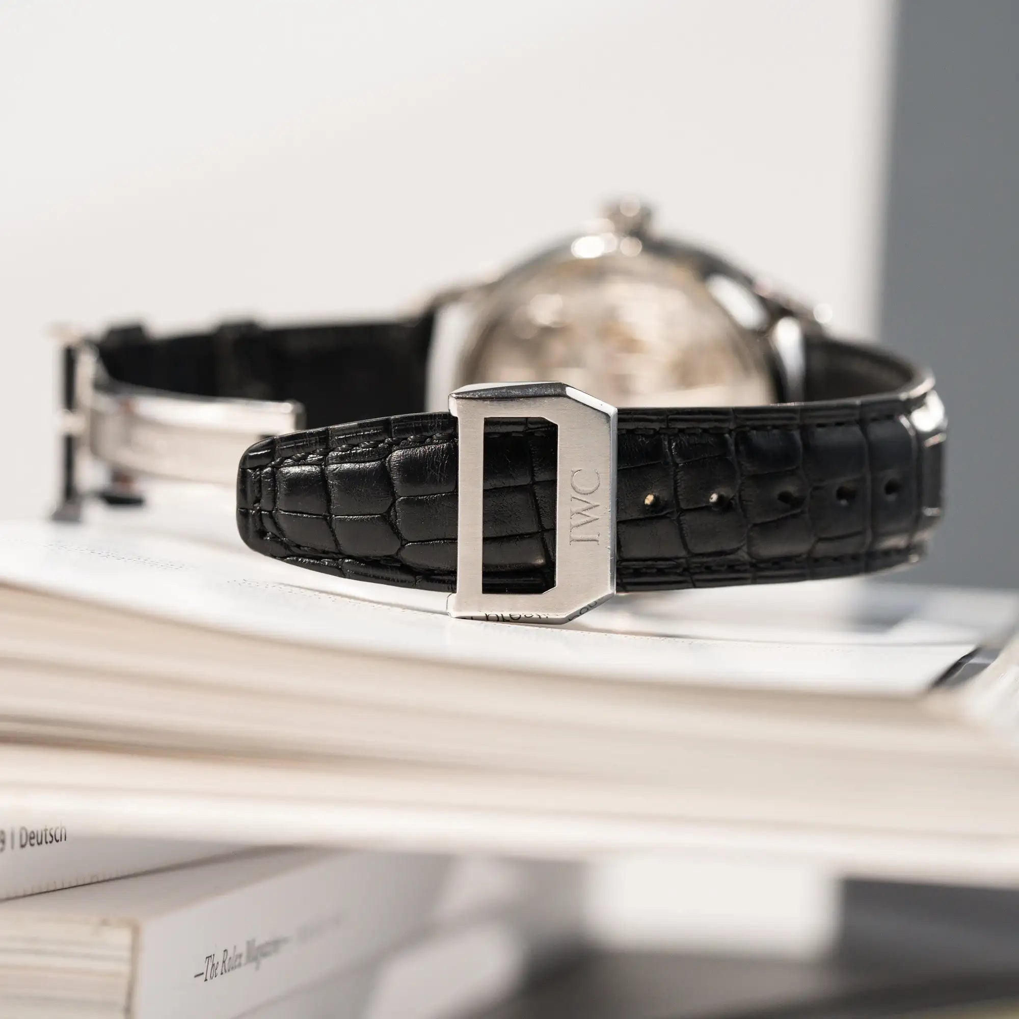 Produktfotografie der seitlich liegenden Portugieser 7 Days Automatic IW500109 Uhr von IWC Schaffhausen am schwarzen Lederband mit Blick auf die IWC-Faltschließe