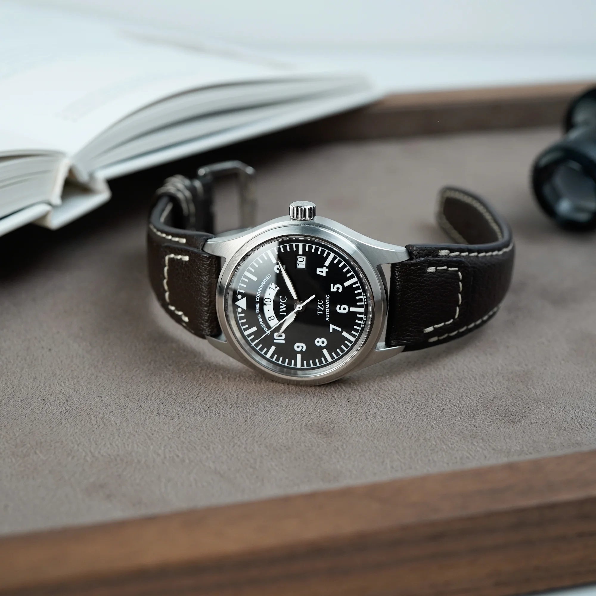 IWC Schaffhausen Pilot Fliegeruhr UTC Spitfire mit der Referenz IW3251 am braunen Lederarmband liegt mit offener Schließe auf hellbraunem Tablet