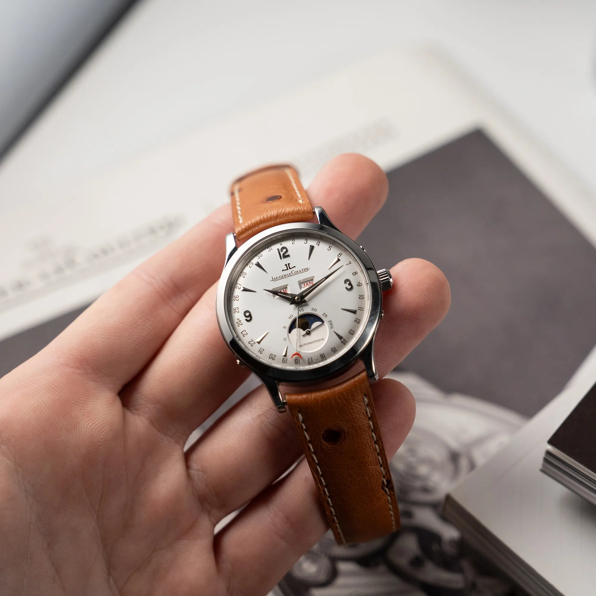 Mann präsentiert der Kamera die Jaeger LeCoultre Master Control Calender Moonphase mit silbernem Zifferblatt an einem braunen JLC_Lederband