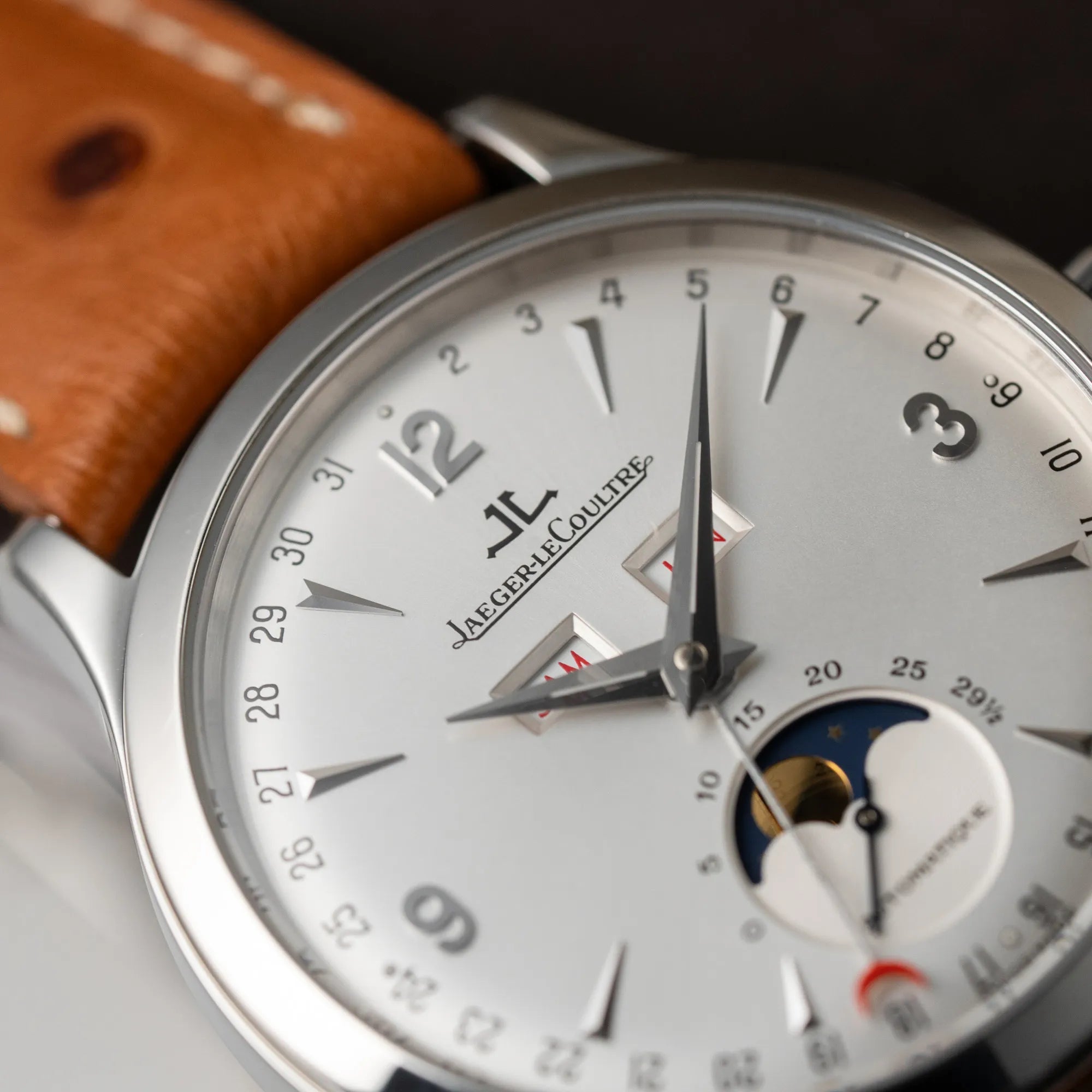 Detailaufnahme mit Fokus auf dem Zeigersatz der Jaeger LeCoultre Master Control Calender Moonphase mit silbernem Zifferblatt an einem braunen JLC-Lederband