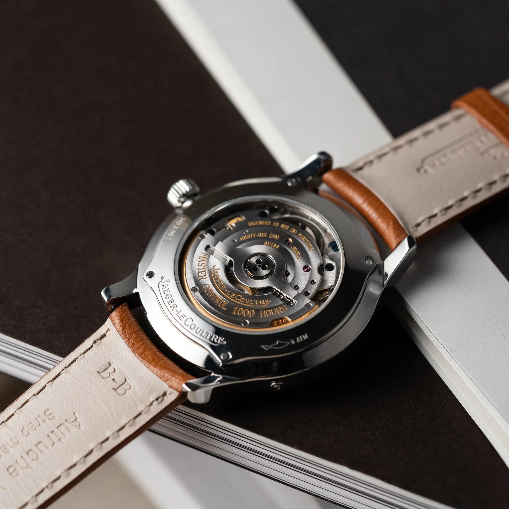 Produktfotografie der Jaeger LeCoultre Master Control Calender Moonphase mit silbernem Zifferblatt an einem braunen JLC-Lederband mit Blick auf den Glasboden