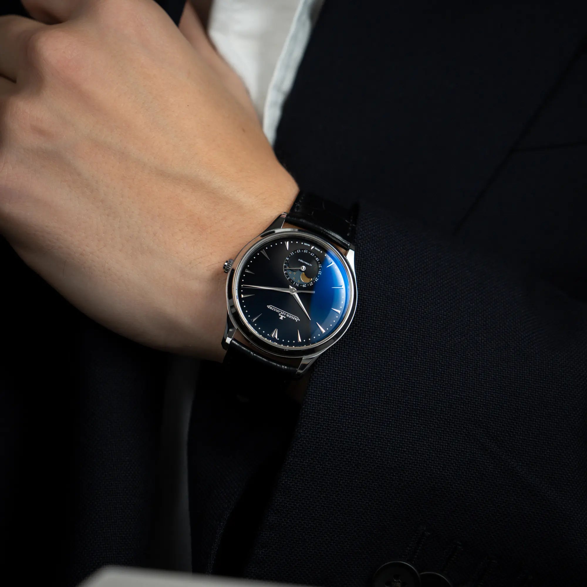 Mann in blauem Sakko trägt die Jaeger-LeCoultre Master Control Q1368470 mit Datum und Mondphase in der schwarzen Zifferblattvariante für einen Wristshot an seinem Handgelenk