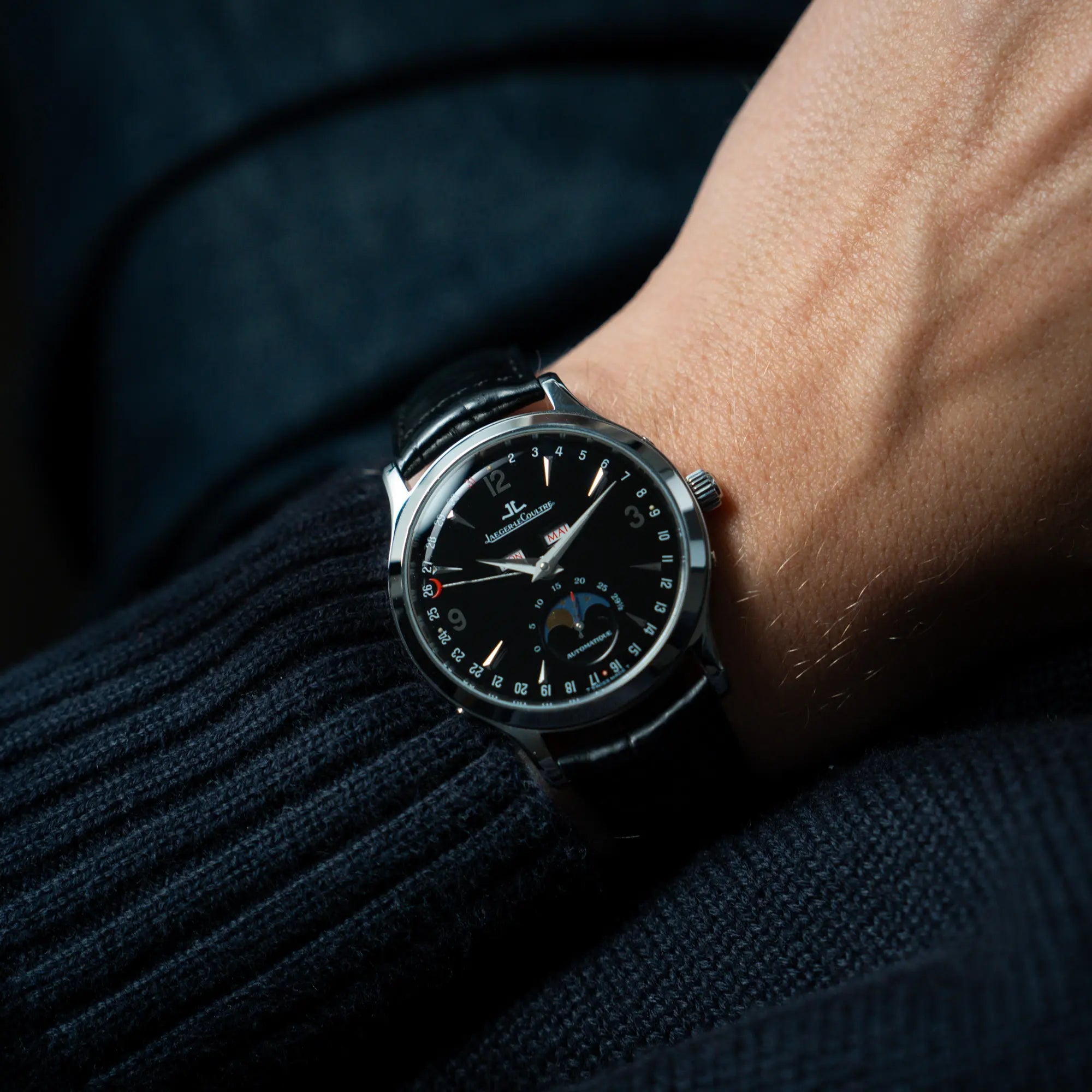 Mann trägt die Jaeger-LeCoultre Master Control Moonphase Calendar mit schwarzem Zifferblatt am schwarzen Lederband für einen Wristshot an seinem Handgelenk