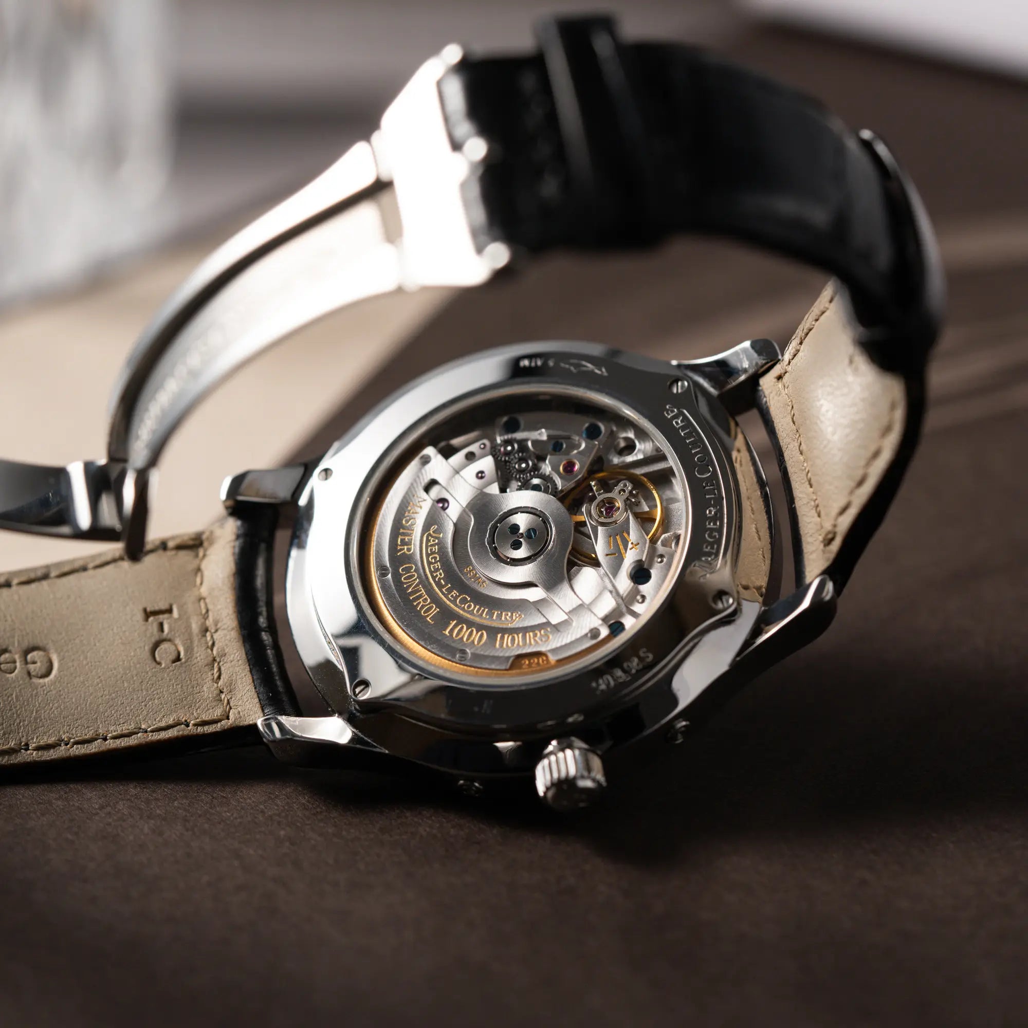 Produktfotografie zeigt den gläsernen Gehäuseboden mit Blick auf das Uhrwerk von der Jaeger-LeCoultre Master Control Moonphase Calendar mit schwarzem Zifferblatt am schwarzen Lederband