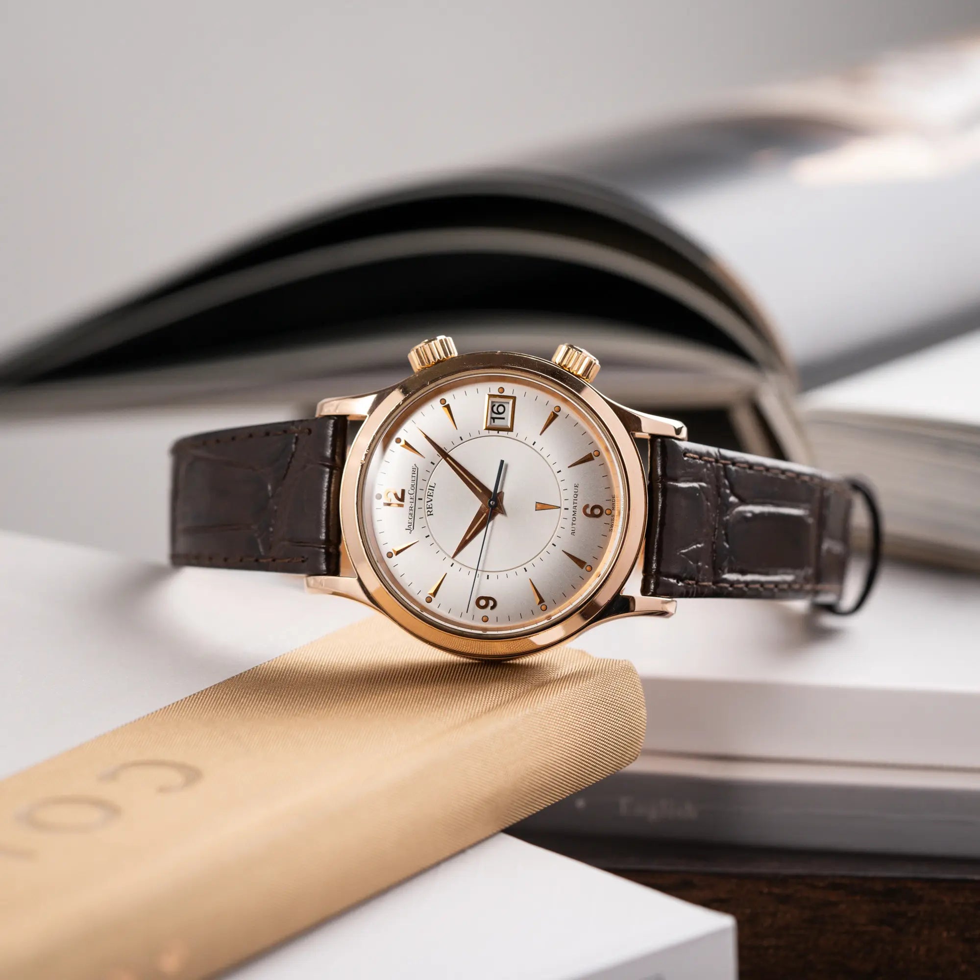 Produktfotografie der seitlich auf dem Uhrengehäuse liegenden Jaeger-LeCoultre Master Memovox 141.2.97 Armbanduhr in Rosegold mit braunem Lederband