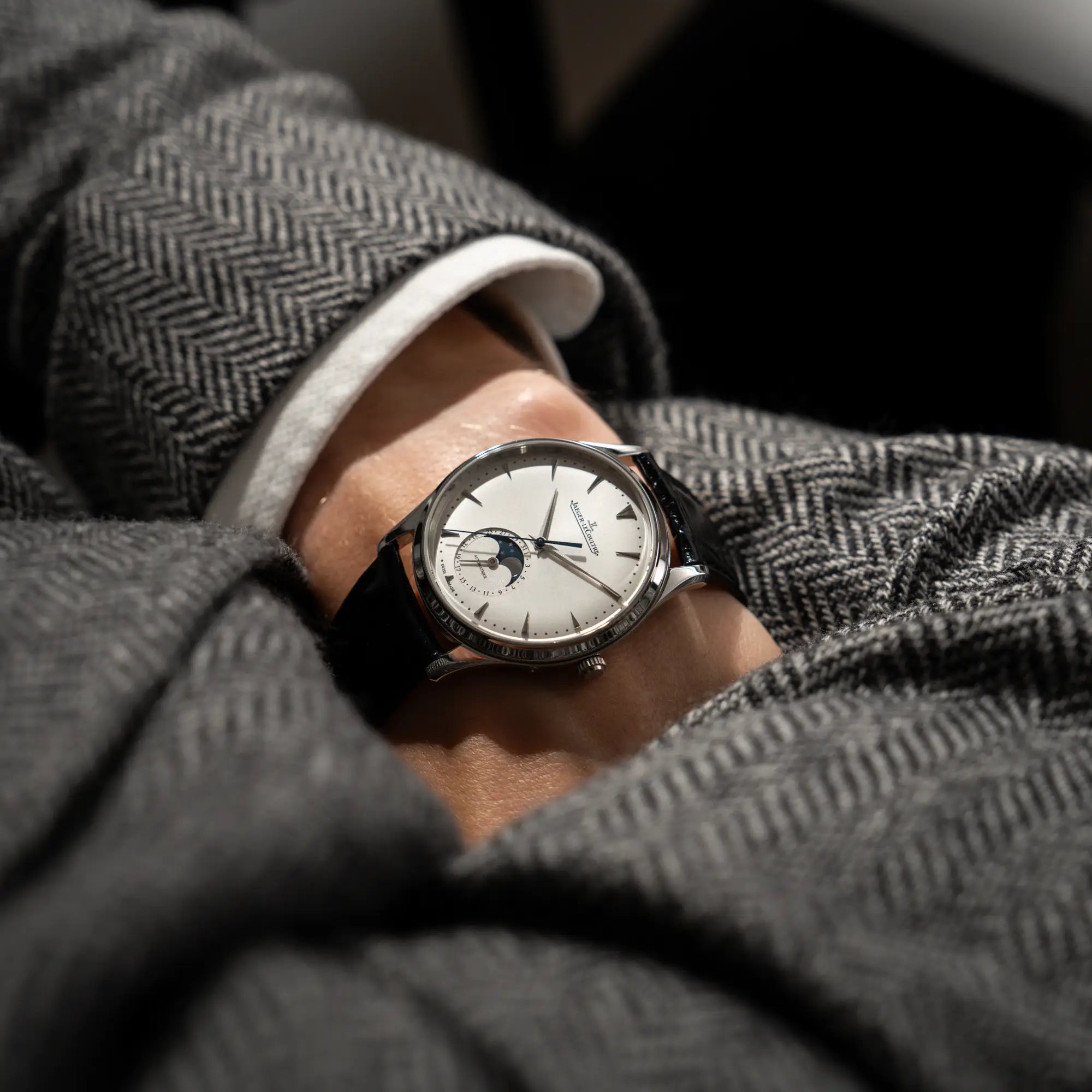 Blick über die Schulter eines Mannes, der die Jaeger-LeCoultre Master Ultra Thin mit Mondphase der Referenz 176.8.64.S mit weiß-silbernem Zifferblatt an seinem Handgelenk