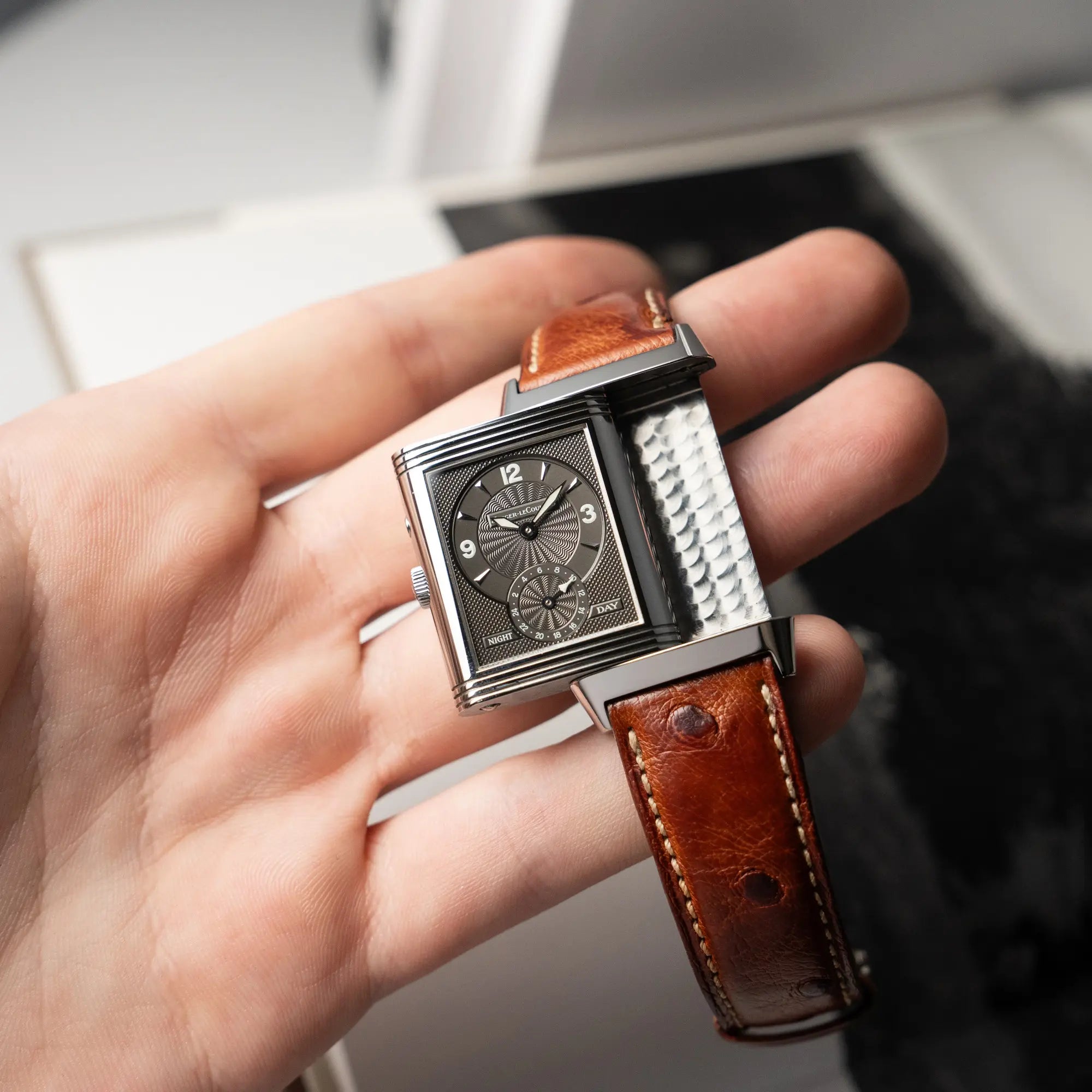 Mann hält die JLC Reverso Duoface 270.8.54 am braunen Lederband in seinen Hand, während der Reverso-Mechanismus in Benutzung ist