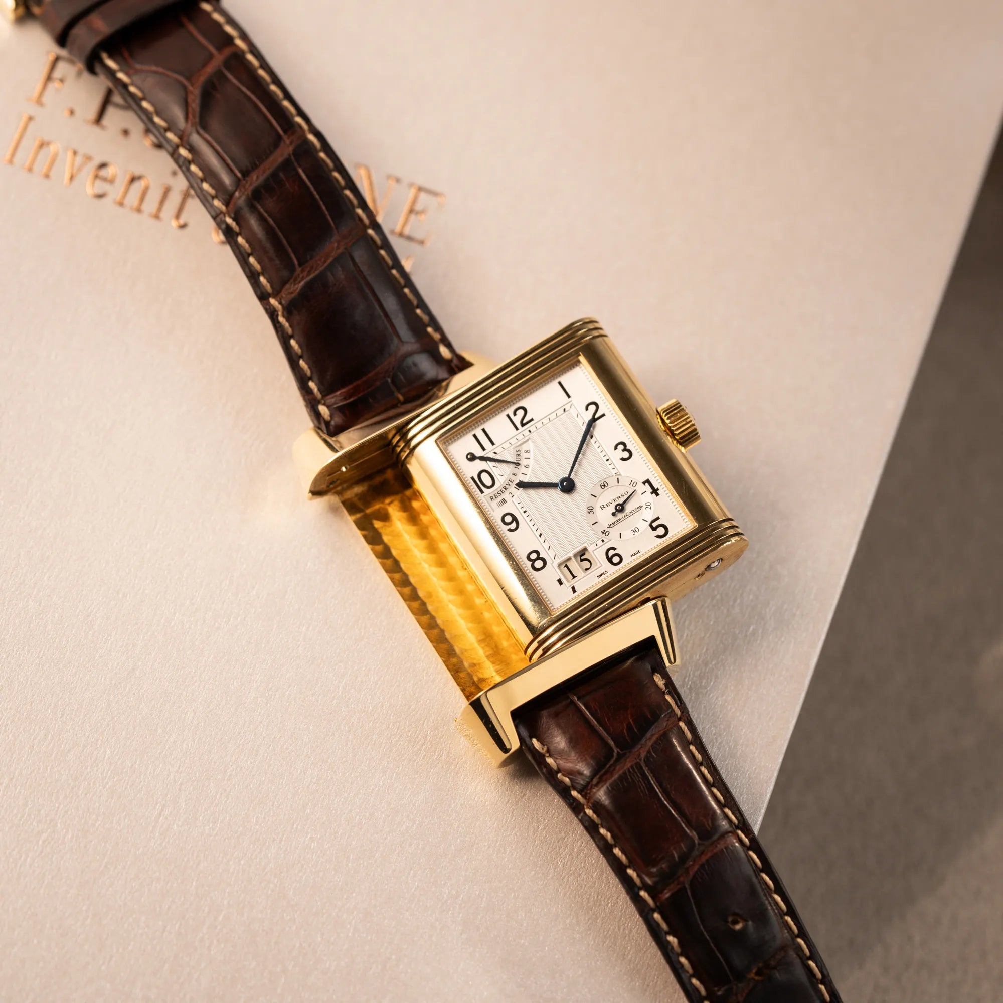 Produktfotografie der Jaeger-LeCoultre Reverso Grande Date der Referenz 240.1.15 mit einem Gelbgold-Gehäuse am braunen Lederband während der Reverso-Mechanismus betätigt wurde