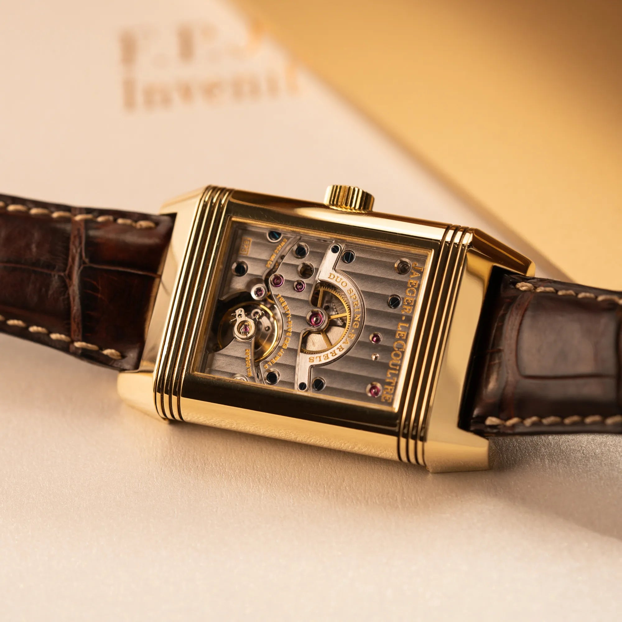 Detailaufnahme des Uhrenkopfes mit umgedrehten Reverso-Mechanismus der Jaeger-LeCoultre Reverso Grande Date der Referenz 240.1.15 mit einem Gelbgold-Gehäuse am braunen Lederband ermöglicht den Blick auf das Uhrwerk durch den Sichtboden aus Glas