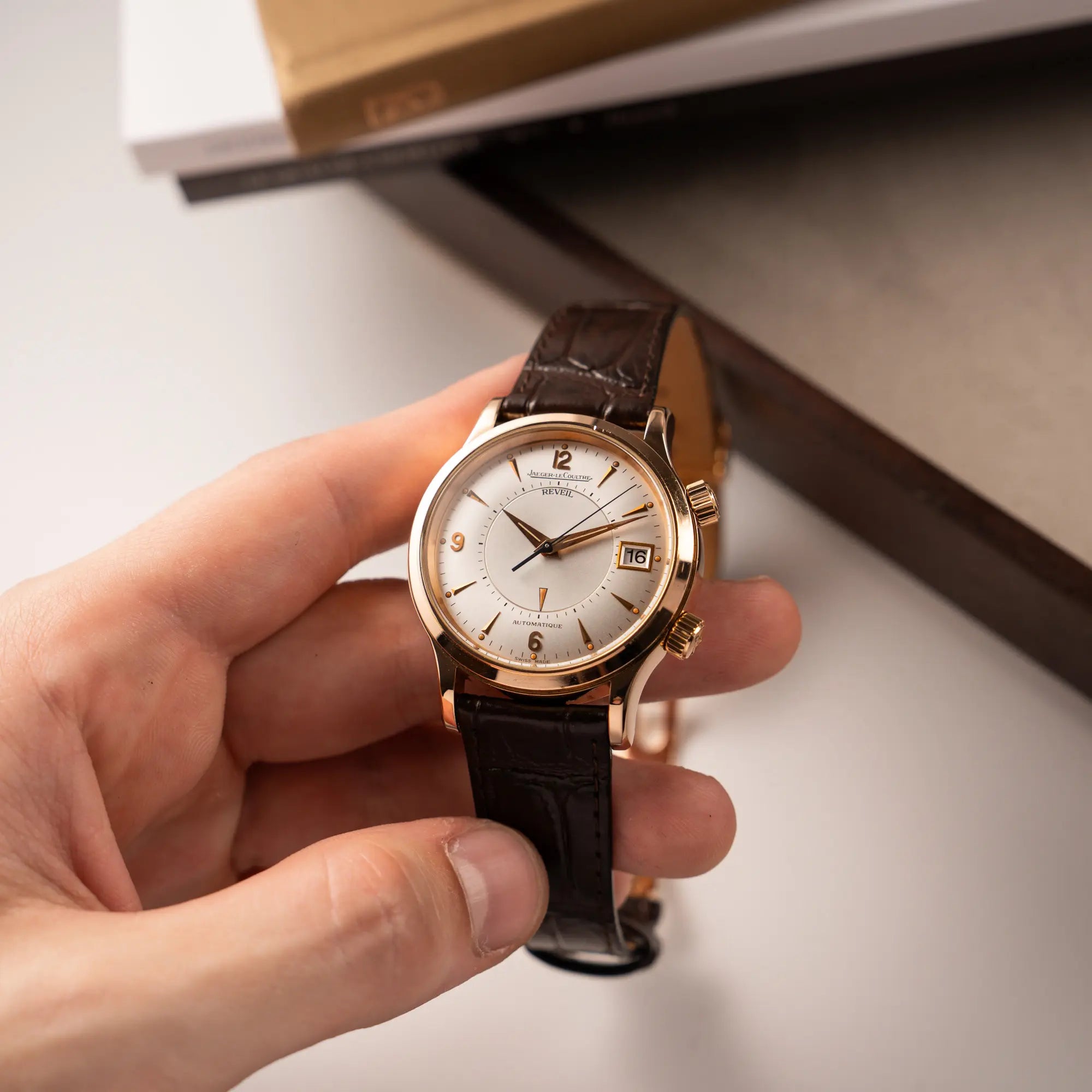 Mann hält die Jaeger-LeCoultre Master Memovox 141.2.97 Armbanduhr in Rosegold mit braunem Lederband in seiner Hand und präsentiert die Uhr in die Kamera