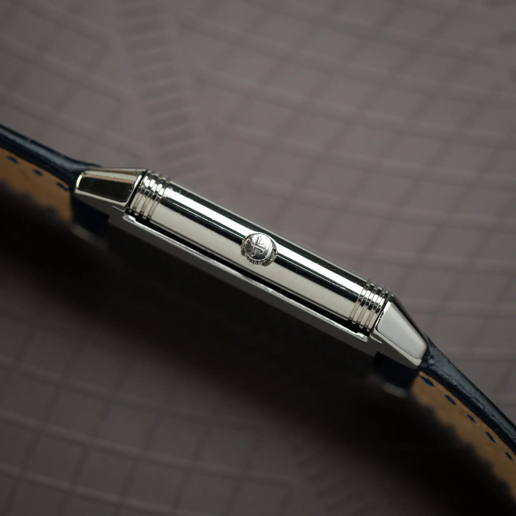 Produktfotografie der Jaeger-LeCoultre Reverso Classique Medium 250.8.86 in Edelstahl an einem dunkelblauem Lederband zeigt die Gehäuseflanke mit Aufzugskrone