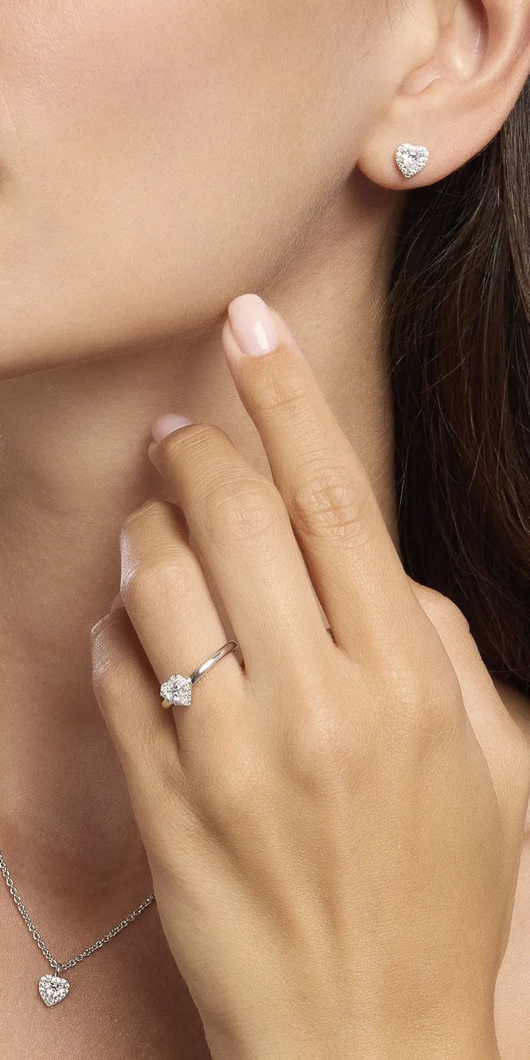 Frau trägt einen silbernen Ohrstecker in Herzform mit Steinbesatz von Mabina und dazu den passenden Ring und eine Halskette mit entsprechendem Angebot