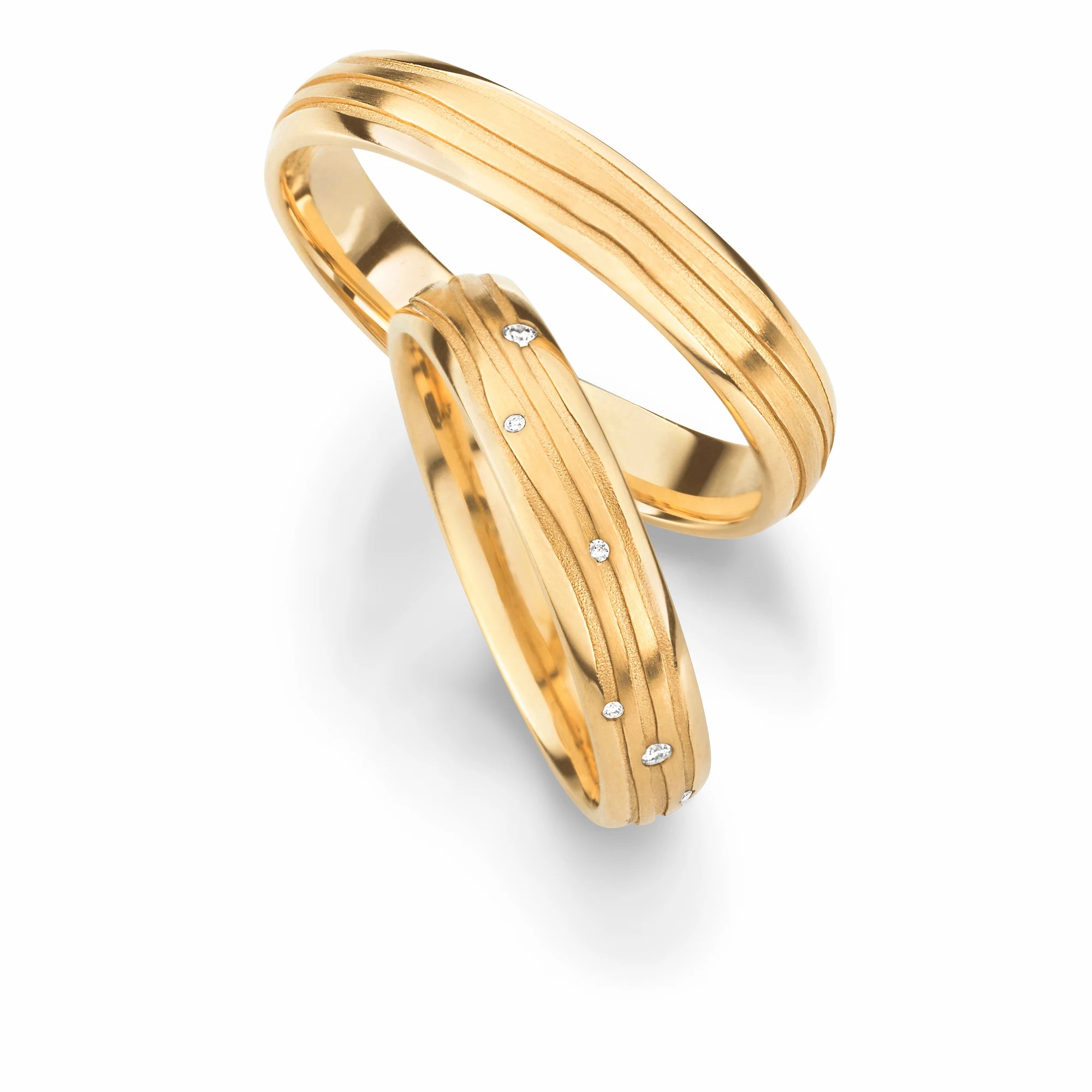 Produktfotografie des gelbgoldenen Max Kemper Trauringpaars mit 3 organisch verlaufenden, eingravierten Linien als Oberflächenstruktur und Diamanten als Verzierung des Damenrings