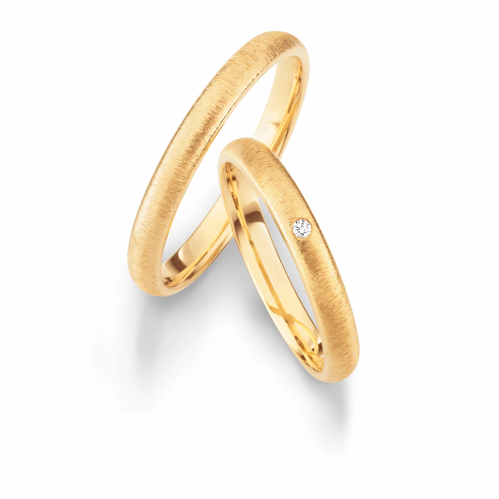 Produktfotografie des gelbgoldenen Max Kemper Trauringpaars mit einer quer verlaufenden, gebürsteten Oberflächen-Beschaffenheit und einem Diamant als Verzierung im Damenring