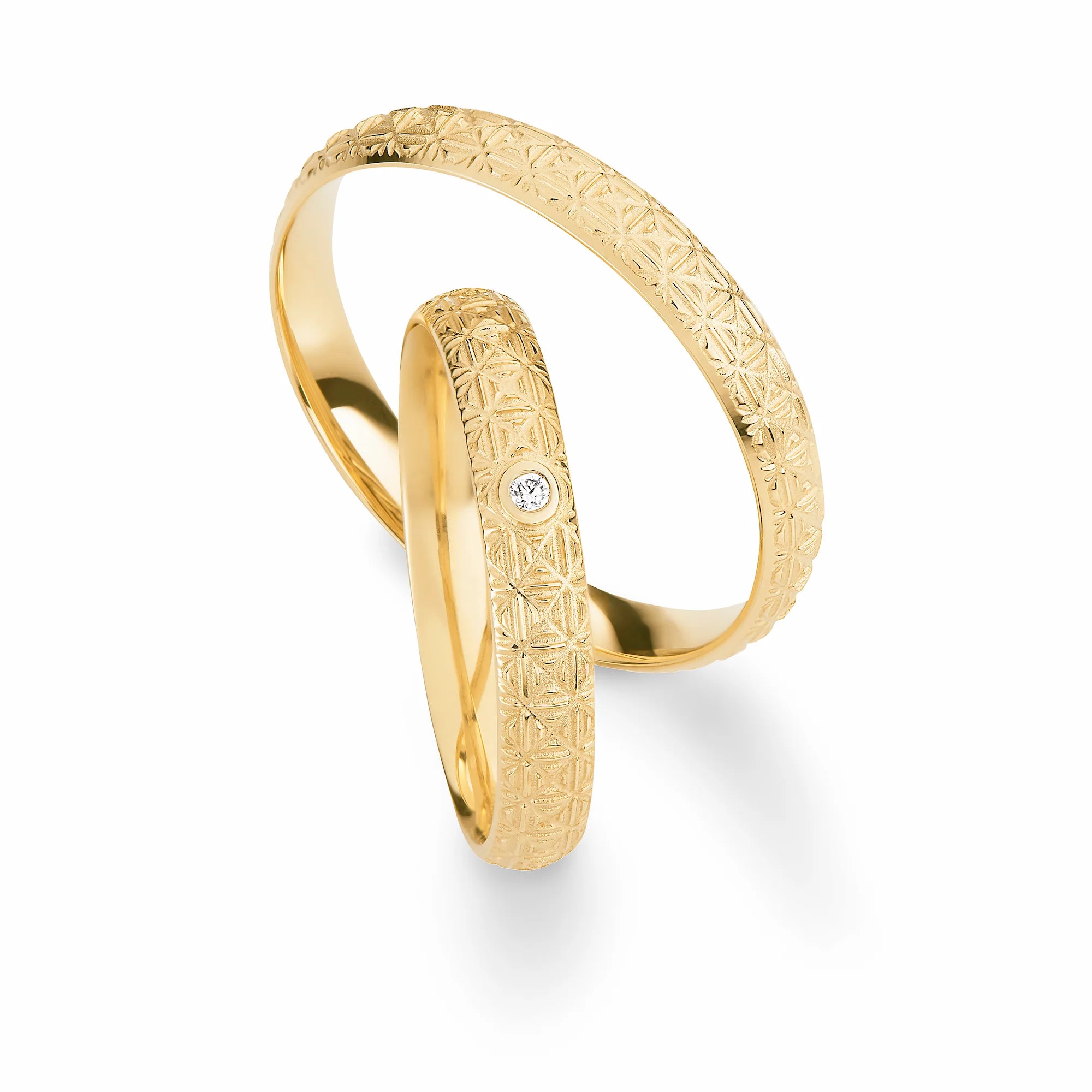 Produktfotografie des gelbgoldenen Max Kemper Trauringpaars mit sehr fein gemusterter symmetrischer Oberflächenstruktur und einem zentral gefassten Brillanten als Verzierung des Damenrings