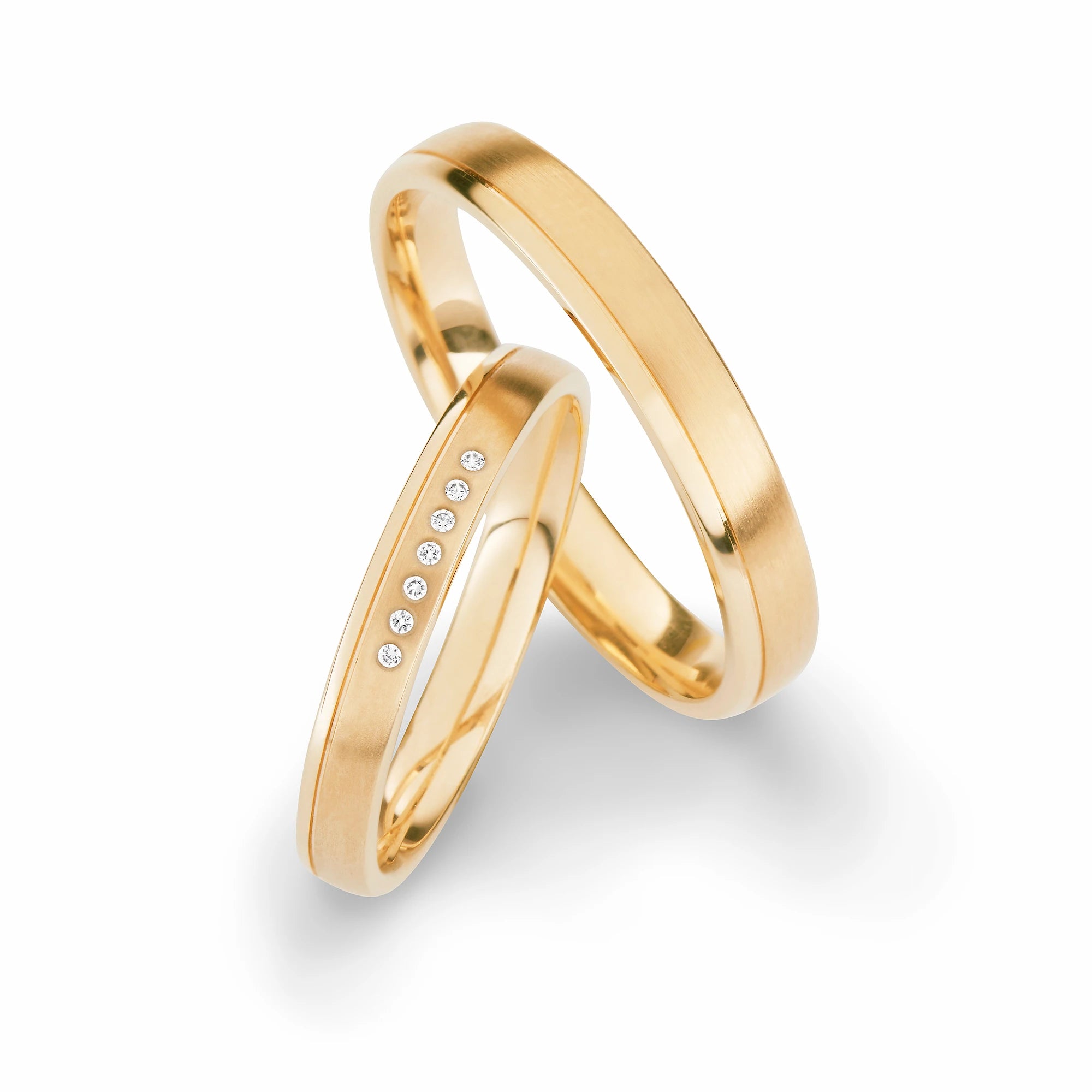 Produktfotografie des gelbgoldenen Max Kemper Trauringpaars mit einer leicht versetzen zentralen Phase und Diamanten im Damenring