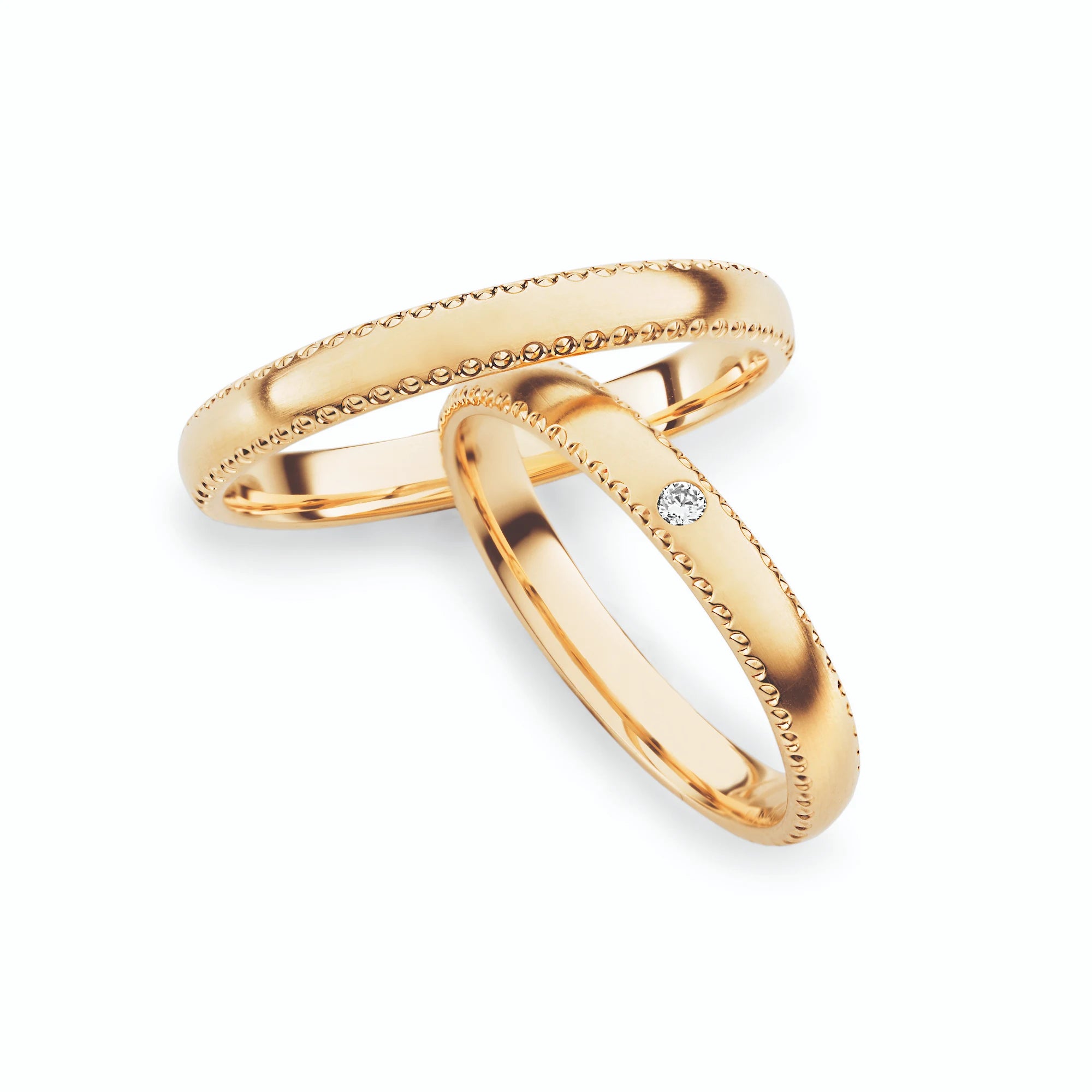 Produktfotografie des gelbgoldenen Max Kemper Trauringpaars mit polierter Oberfläche und ornamentartiger Verzierung an den Aussenseiten des Rings , sowie einem Brillanten als Verzierung des Damenrings