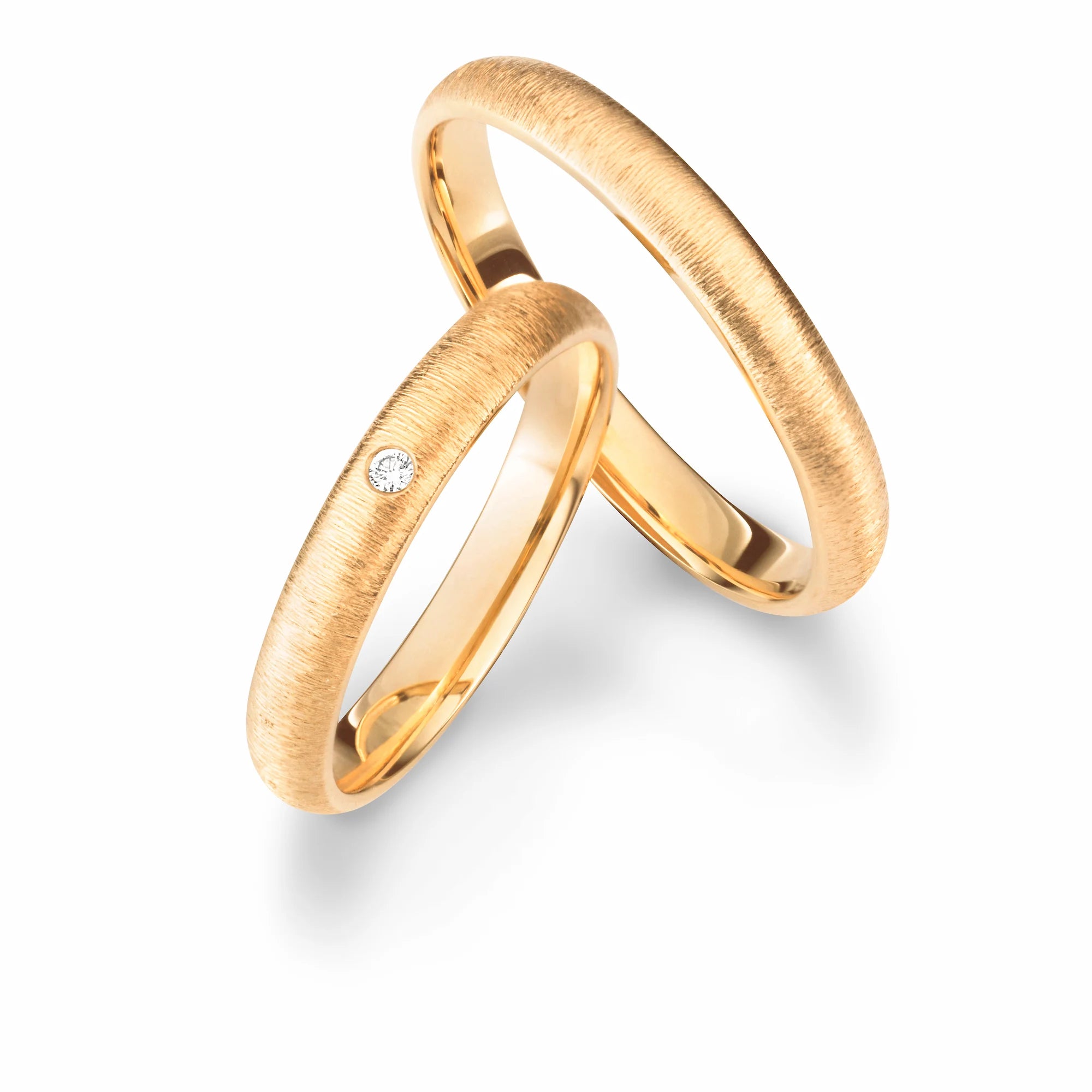 Produktfotografie des gelbgoldenen Max Kemper Trauringpaars mit einer zur Ringschiene quer verlaufenden, gebürsteten Oberflächenstruktur und einem zentralen Diamanten im Damenring