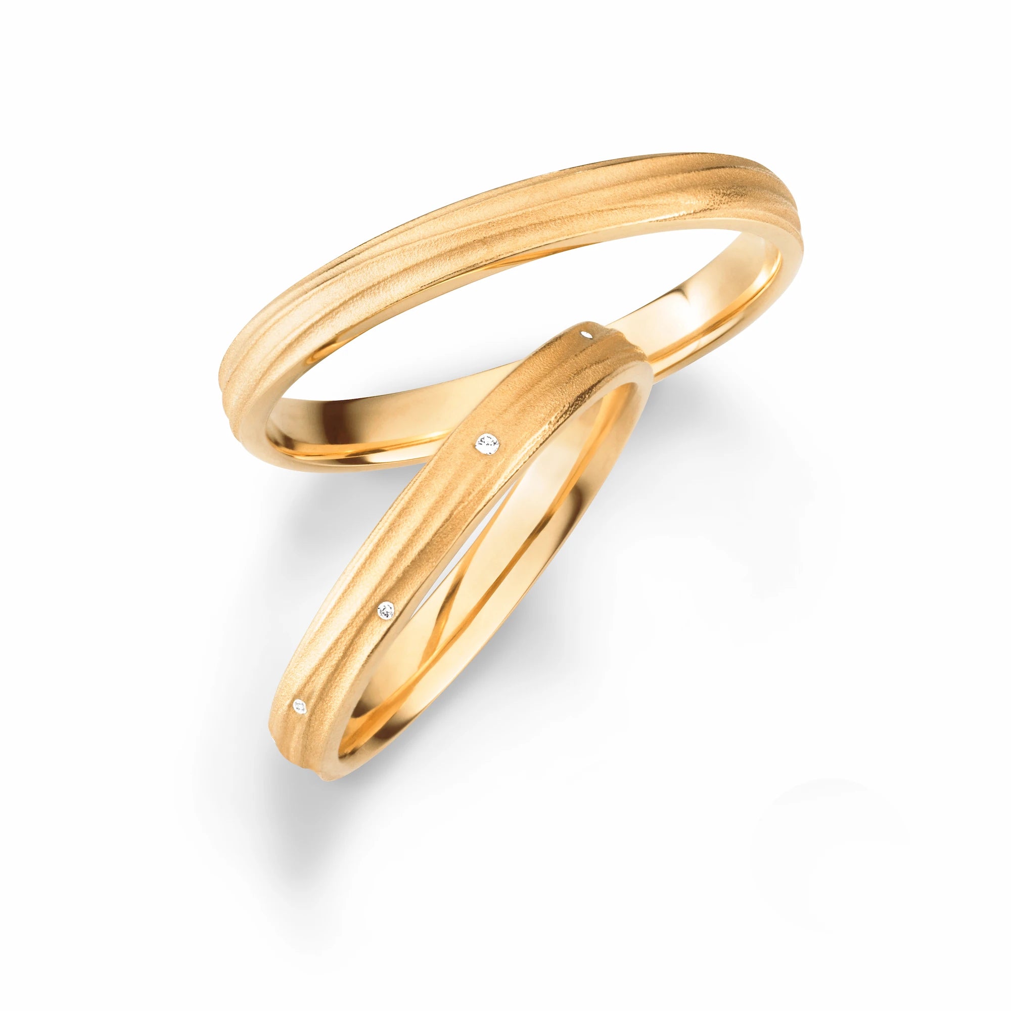 Produktfotografie des gelbgoldenen Max Kemper Trauringpaars mit einer wellenförmig verlaufenden Oberflächenstruktur, die an Baumrinde erinnert, und Diamanten im Damenring