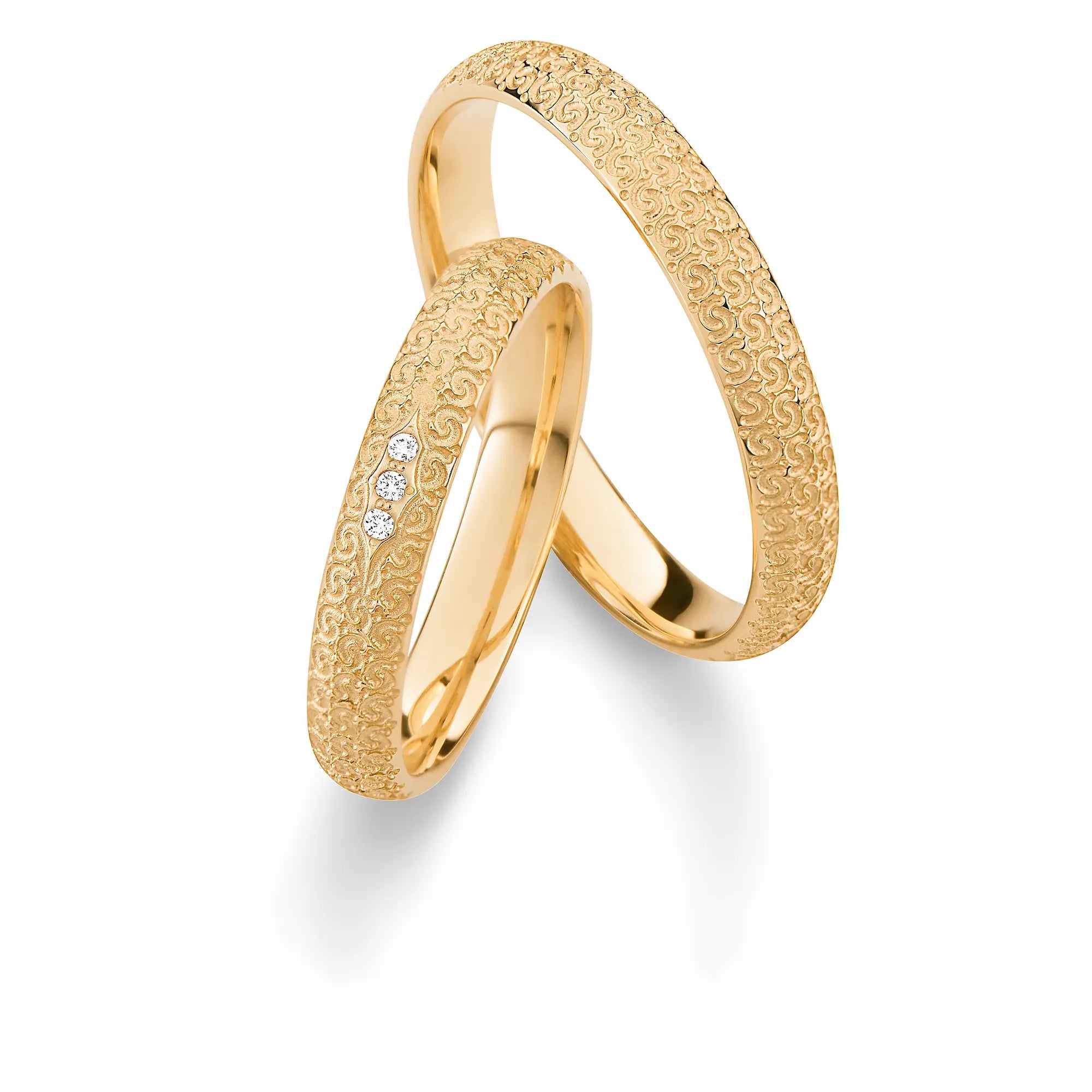 Produktfotografie des gelbgoldenen Max Kemper Trauringpaars mit einer detailreichen, gemusterten, verschnörkelten Oberfläche mit und drei Diamanten im Damenring