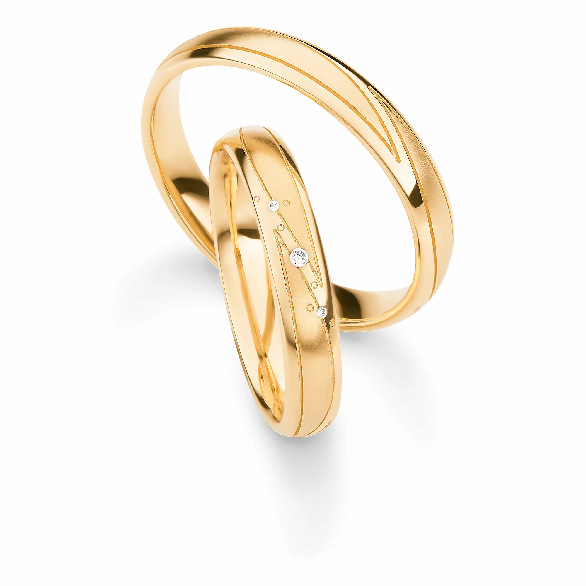 Produktfotografie des gelbgoldenen Max Kemper Trauringpaars mit einer glatten, poliertenOberfläche mit eingravierten Nuten und drei passend angeordneten Diamanten im Damenring