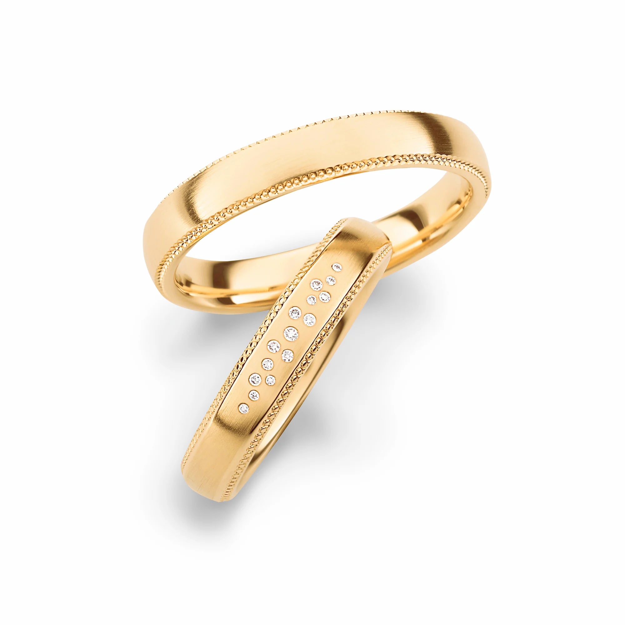 Produktfotografie des gelbgoldenen Max Kemper Trauringpaars mit einer fein strukturierten Oberfläche und einer detailreichen Verzierung an der Außenkante und Diamanten im Damenring