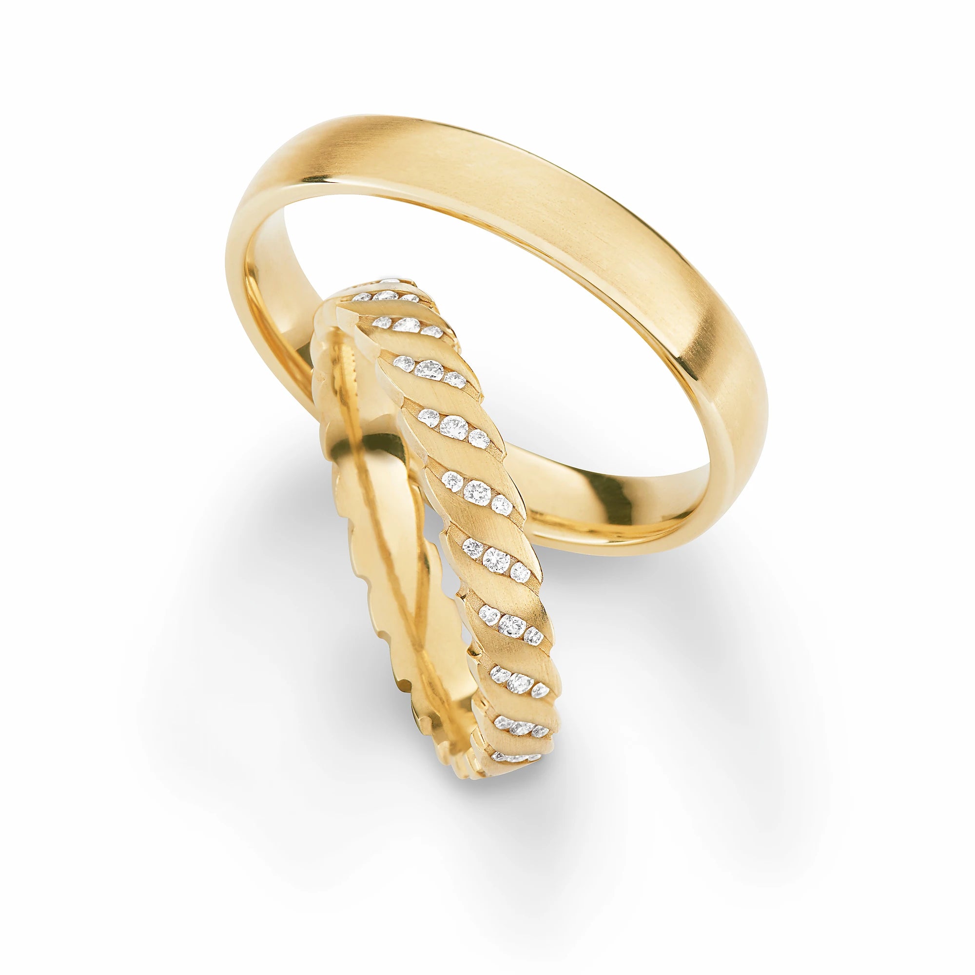 Produktfotografie des gelbgoldenen Max Kemper Trauringpaars mit einer fein strukturierten Oberflächenstruktur und schräg angeordneten Diamanten-Reihen auf der Ringschiene des Damenrings jeweils bestehend aus 3er-Sets an Brillanten