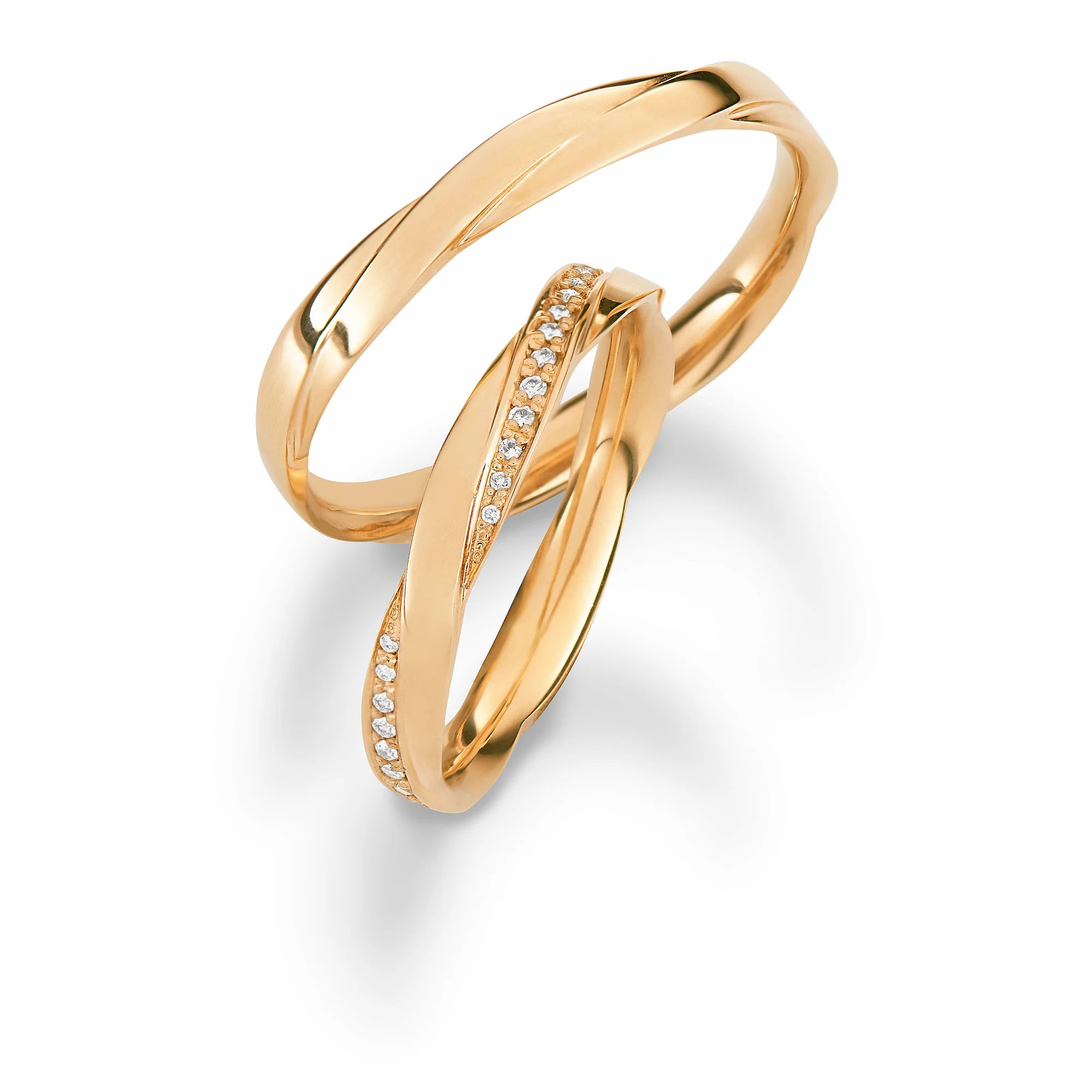 Produktfotografie des gelbgoldenen Max Kemper Trauringpaars mit einer einzigartigen Form derfümmen Ringschiene, die an zwei ineinander verschmelzende Ringe erinnert, mit einer polierten Oberfläche und speziell für den Damenring eingefassten Diamant-Schienen