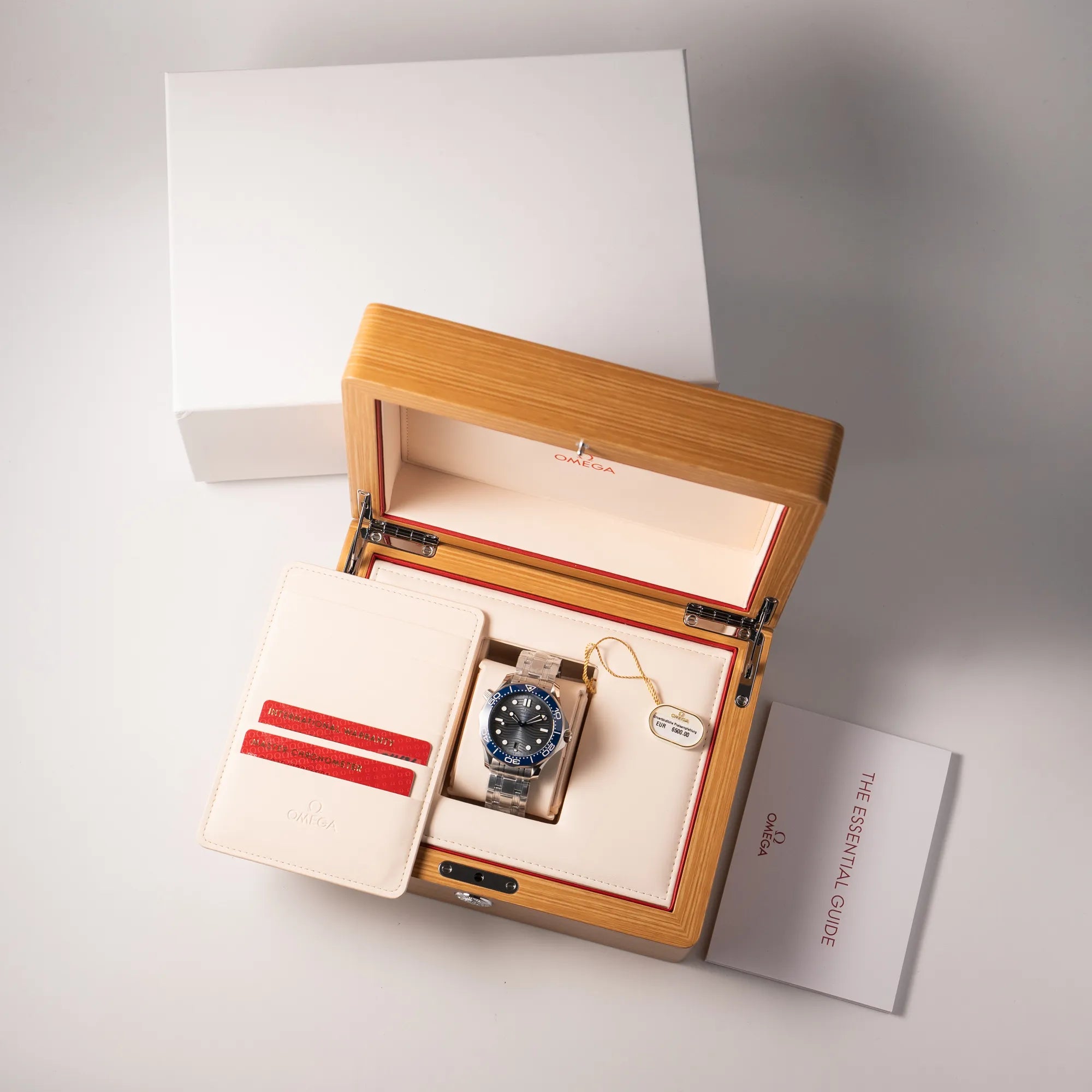Lieferumfang zugehörig zu der Omega Seamaster Diver 300M der Referenz 210.30.42.20.06.001 mit grauem Zifferblatt im Wellen-Design und blauer Lünette am Edelstahlarmband, welches zum Schutz verklebt wurde, bestehend aus Box mit Umkarton, Hangtag, Garantiekarte und Booklets