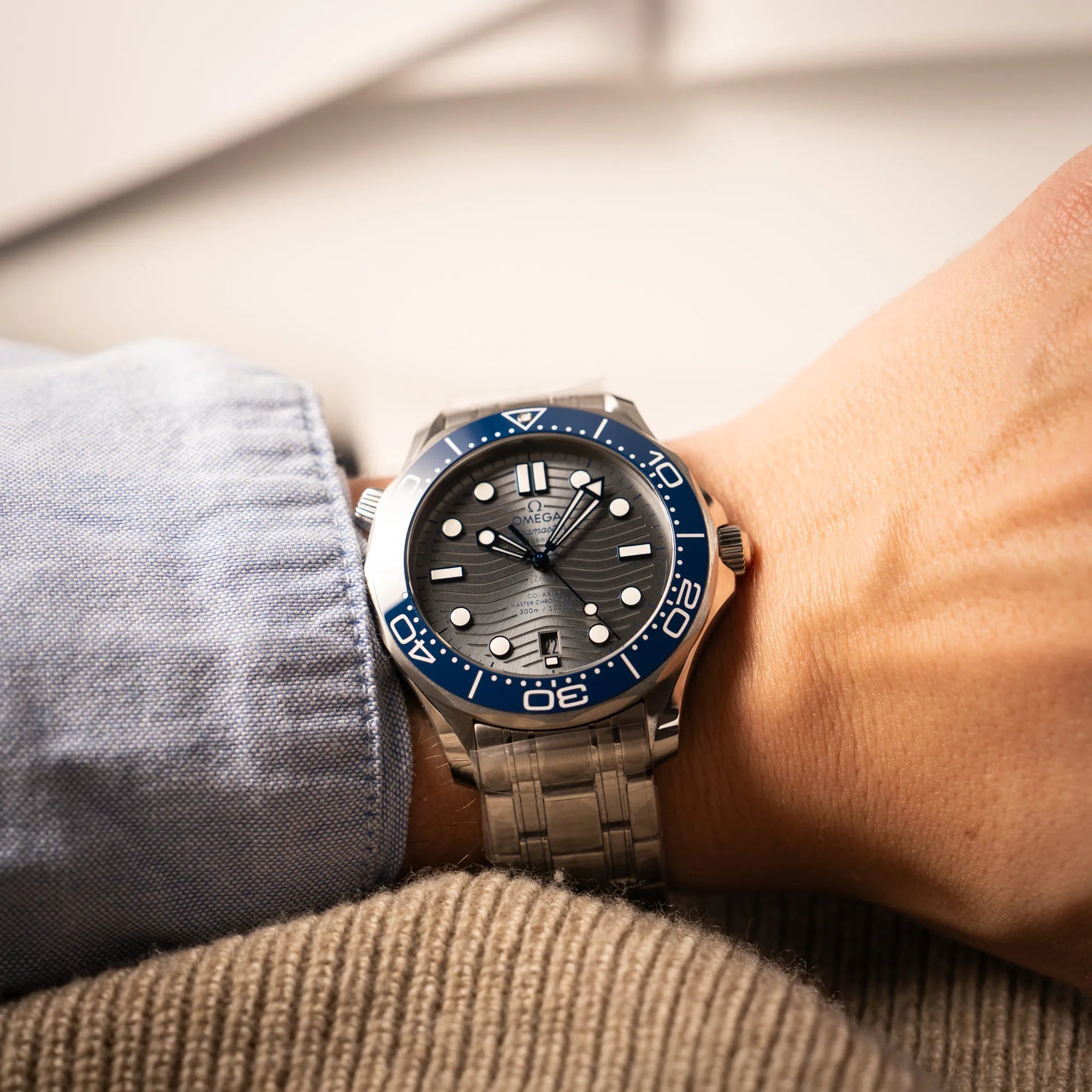 Mann trägt die Omega Seamaster Diver 300M der Referenz 210.30.42.20.06.001 mit grauem Zifferblatt im Wellen-Design und blauer Lünette am Edelstahlarmband, welches zum Schutz verklebt wurde, an seinem Handgelenk