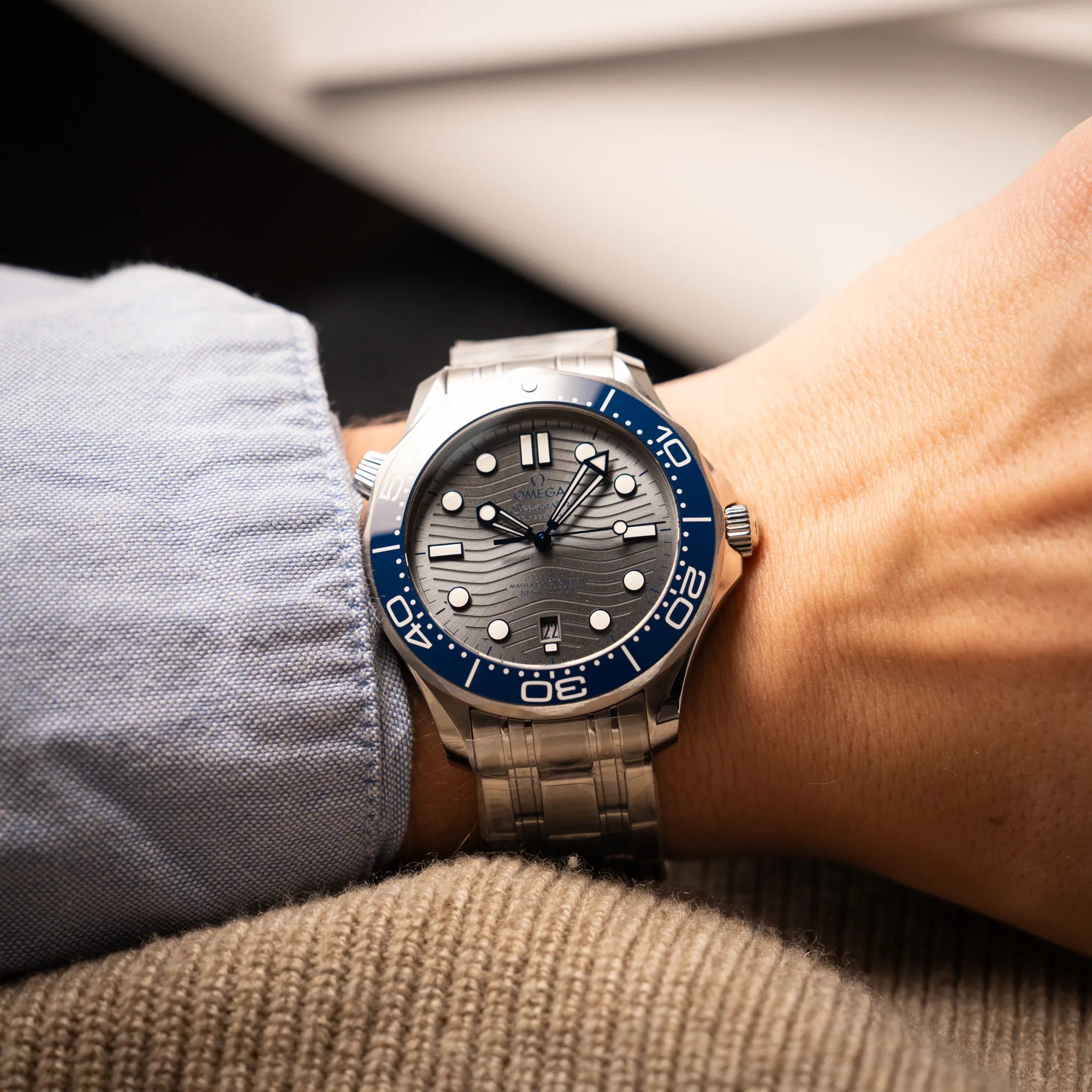 Mann trägt die Omega Seamaster Diver 300M der Referenz 210.30.42.20.06.001 mit grauem Zifferblatt im Wellen-Design und blauer Lünette am Edelstahlarmband, welches zum Schutz verklebt wurde, an seinem Handgelenk