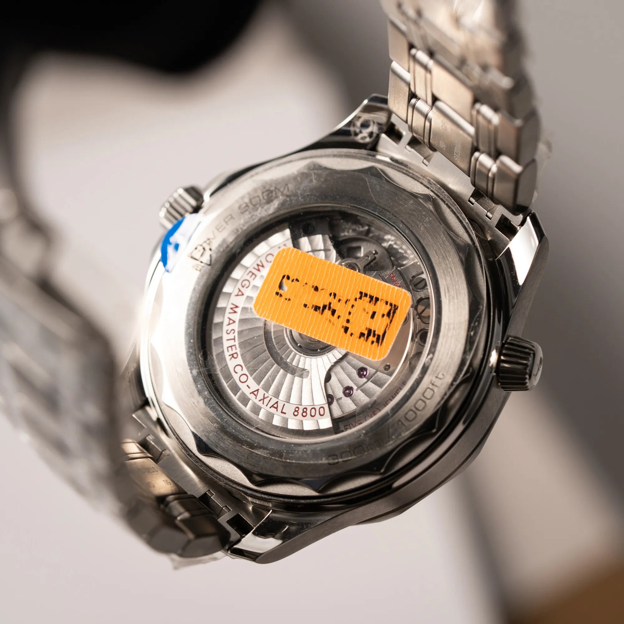 Verklebter Gehäuseboden der Omega Seamaster Diver 300M der Referenz 210.30.42.20.06.001 mit grauem Zifferblatt im Wellen-Design und blauer Lünette am Edelstahlarmband, welches zum Schutz verklebt wurde