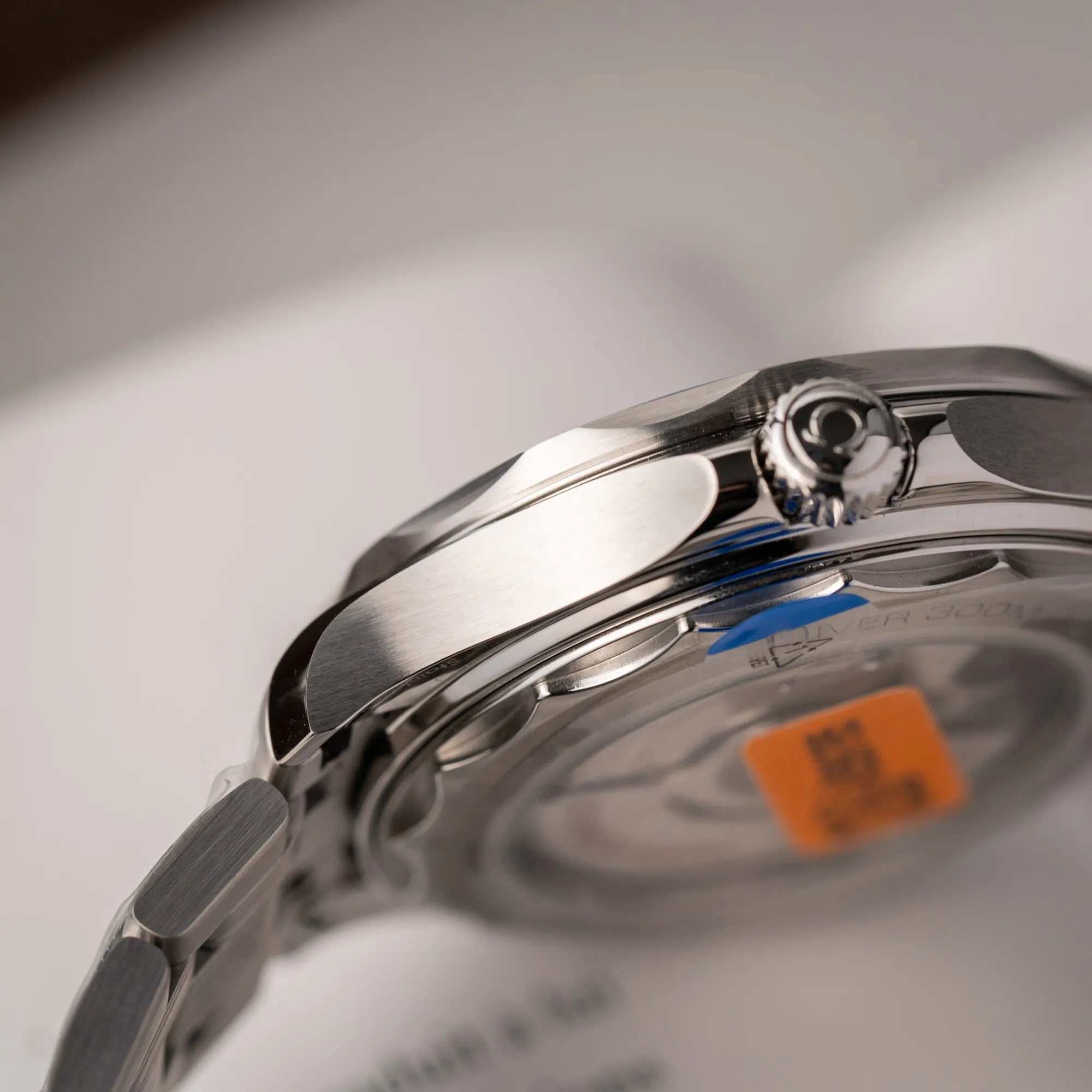 Detailaufnahme der seitlichen Gehäuseflanke der Omega Seamaster Diver 300M der Referenz 210.30.42.20.06.001 mit grauem Zifferblatt im Wellen-Design und blauer Lünette am Edelstahlarmband, welches zum Schutz verklebt wurde