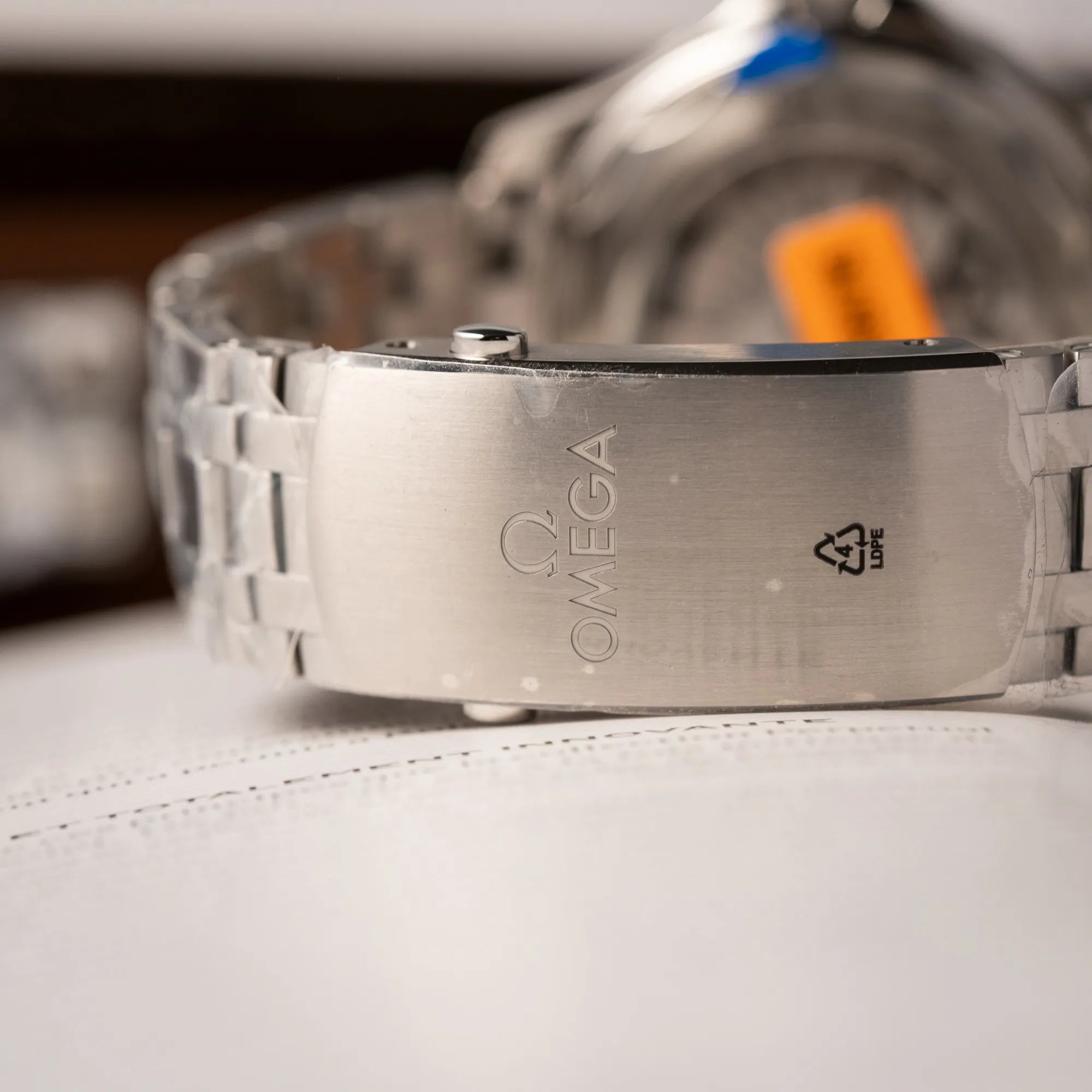 Omega-Faltschliesse der Omega Seamaster Diver 300M der Referenz 210.30.42.20.06.001 mit grauem Zifferblatt im Wellen-Design und blauer Lünette am Edelstahlarmband, welches zum Schutz verklebt wurde