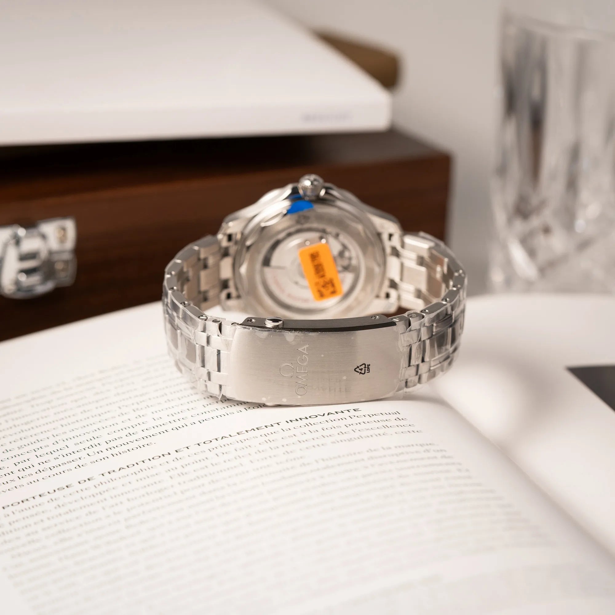 Produktfotografie der Omega Seamaster Diver 300M der Referenz 210.30.42.20.06.001 mit grauem Zifferblatt im Wellen-Design und blauer Lünette am Edelstahlarmband, welches zum Schutz verklebt wurde, zeigt die verklebte Schliesse
