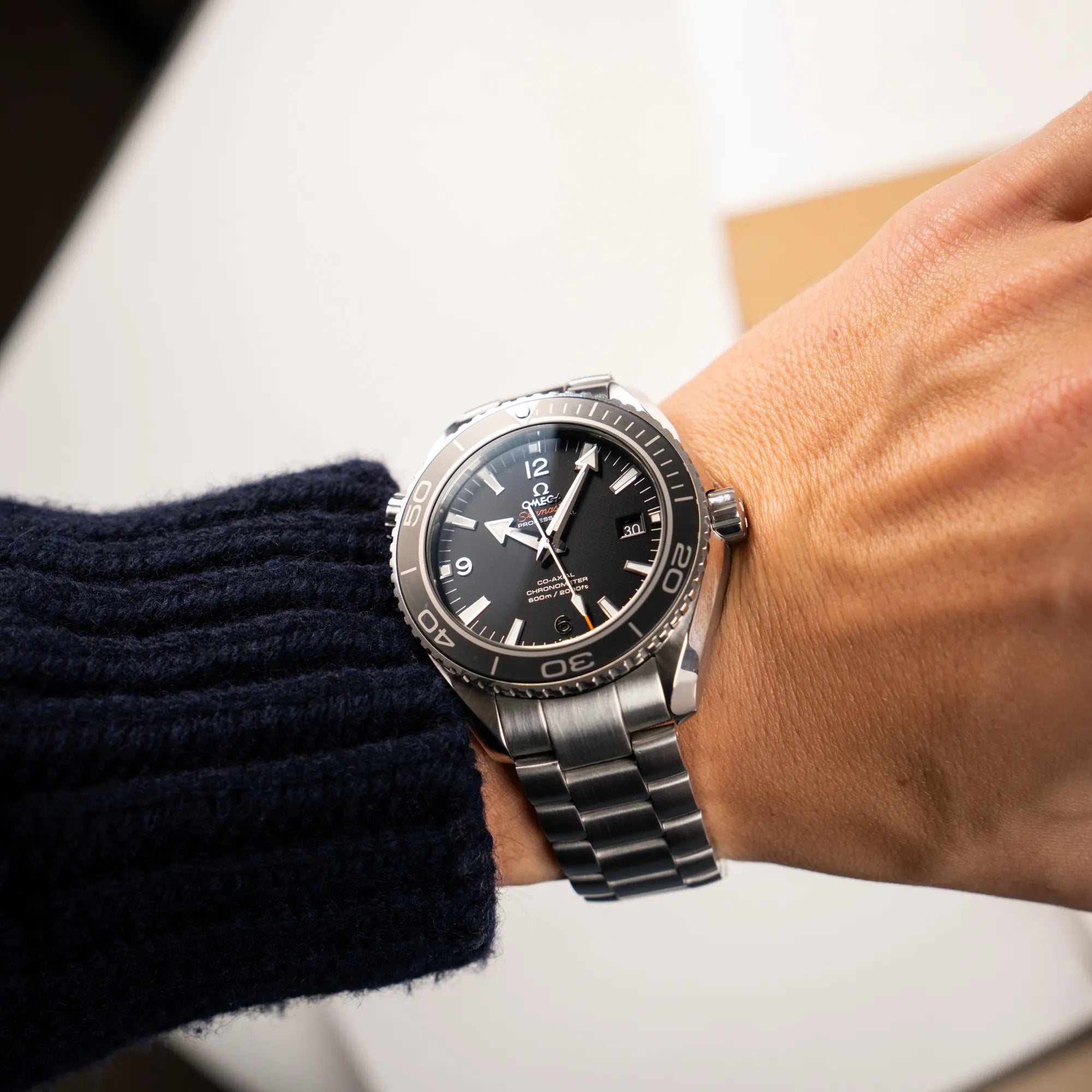 Mann trägt die Omega Seamaster Planet Ocean 232.30.46.21.01.001 mit 45mm Gehäuse und schwarzem Zifferblatt mit orangen Details für einen Wristshot am Hangelenk