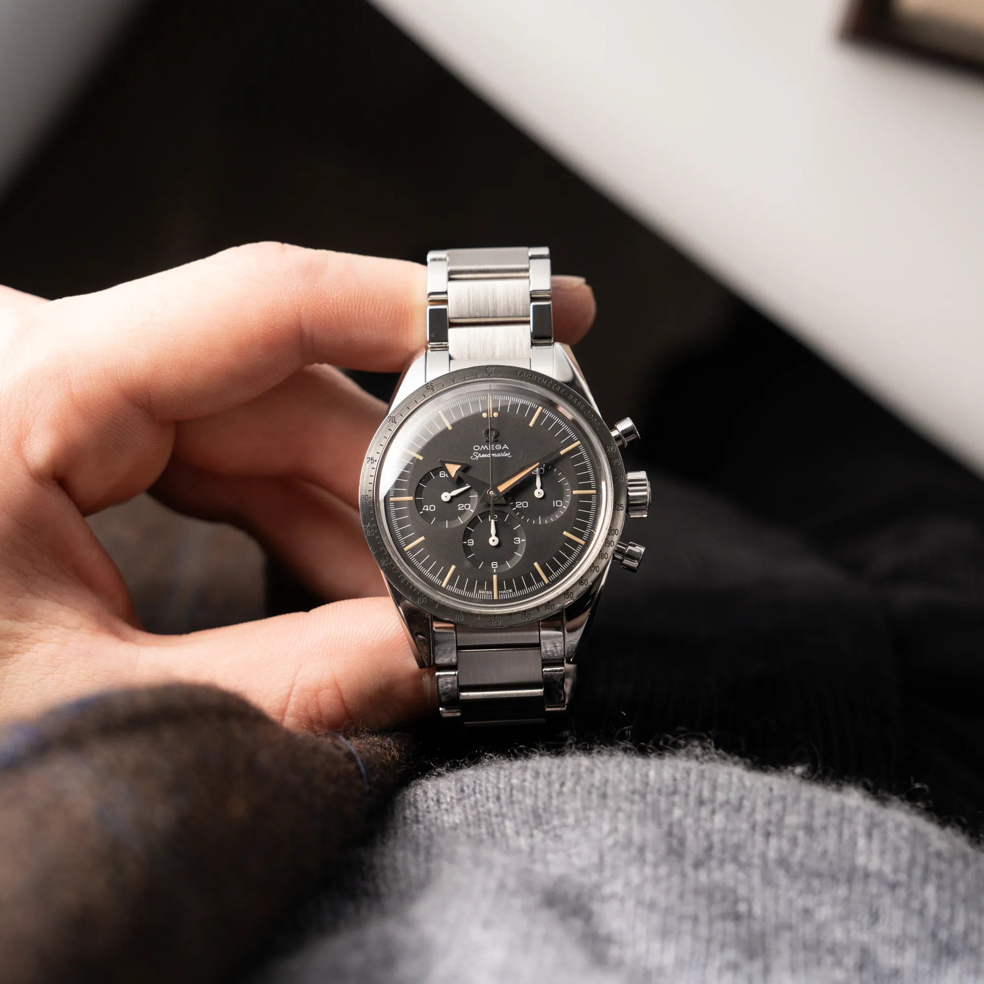 Mann hält die Omega Speedmaster 1957 Trilogy Limited Edition mit einem anthrazitfarbenen Zifferblatt mit Vintage-Look und dem original Omega-Stahlband im Ed-White-Design in seiner Hand und präsentiert die Uhr in die Kamera
