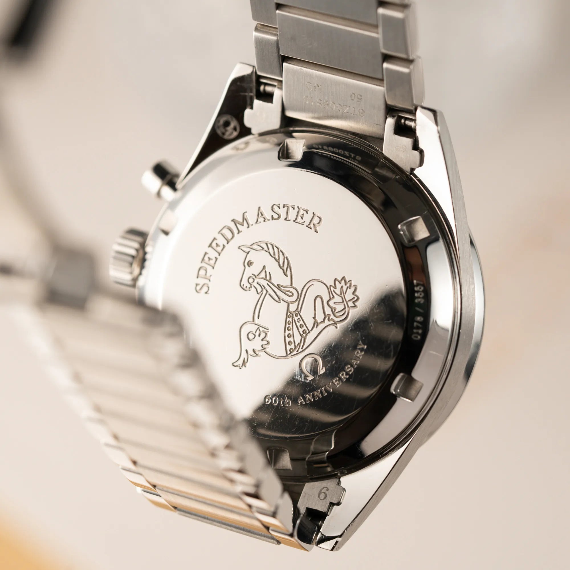 Verschraubter Stahl-Gehäuseboden mit "60th Anniversary" Schriftzug der Omega Speedmaster 1957 Trilogy Limited Edition mit einem anthrazitfarbenen Zifferblatt mit Vintage-Look und dem original Omega-Stahlband im Ed-White-Design