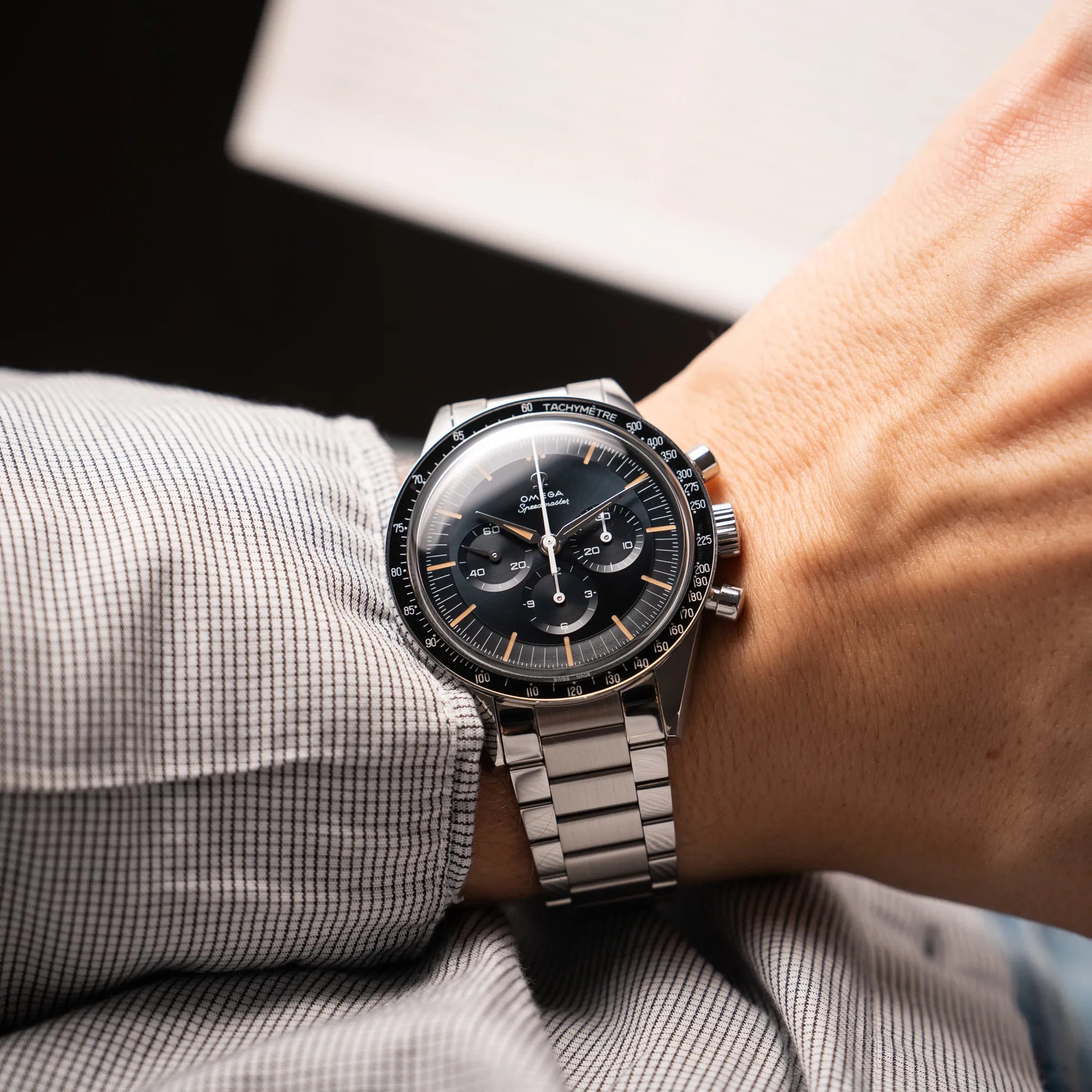Mann trägt die Omega Speedmaster FOIS der Referenz 310.30.40.50.06.001 mit dem dunkelblauen Zifferblatt mit dunkel-beigen Indizes im Vintage-Look und einem vom Standard-Modell abgeänderten Stahl-Armband, was beides an das klassische Speedy-Modell erinnert, an seinem Handgelenk