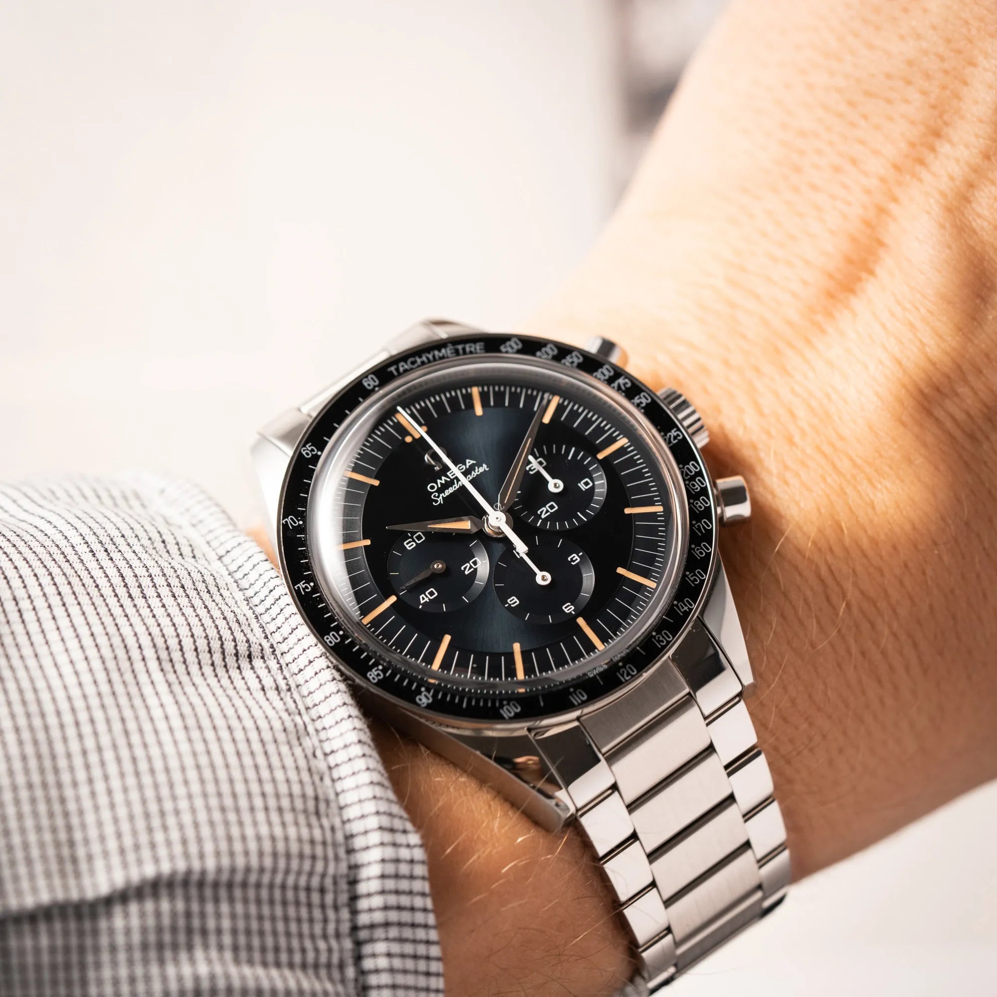 Mann trägt die Omega Speedmaster FOIS der Referenz 310.30.40.50.06.001 mit dem dunkelblauen Zifferblatt mit dunkel-beigen Indizes im Vintage-Look und einem vom Standard-Modell abgeänderten Stahl-Armband, was beides an das klassische Speedy-Modell erinnert, für einen Wristshot an seinem Handgelenk
