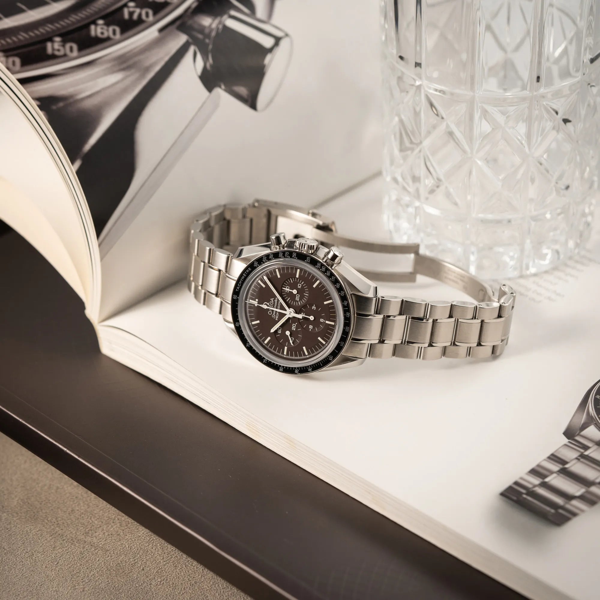 Produktfoto der seitlich auf dem Uhrengehäuse liegenden Omega Speedmaster Professional Moonwatch 311.30.42.30.13.001 mit einem braunen Zifferblatt