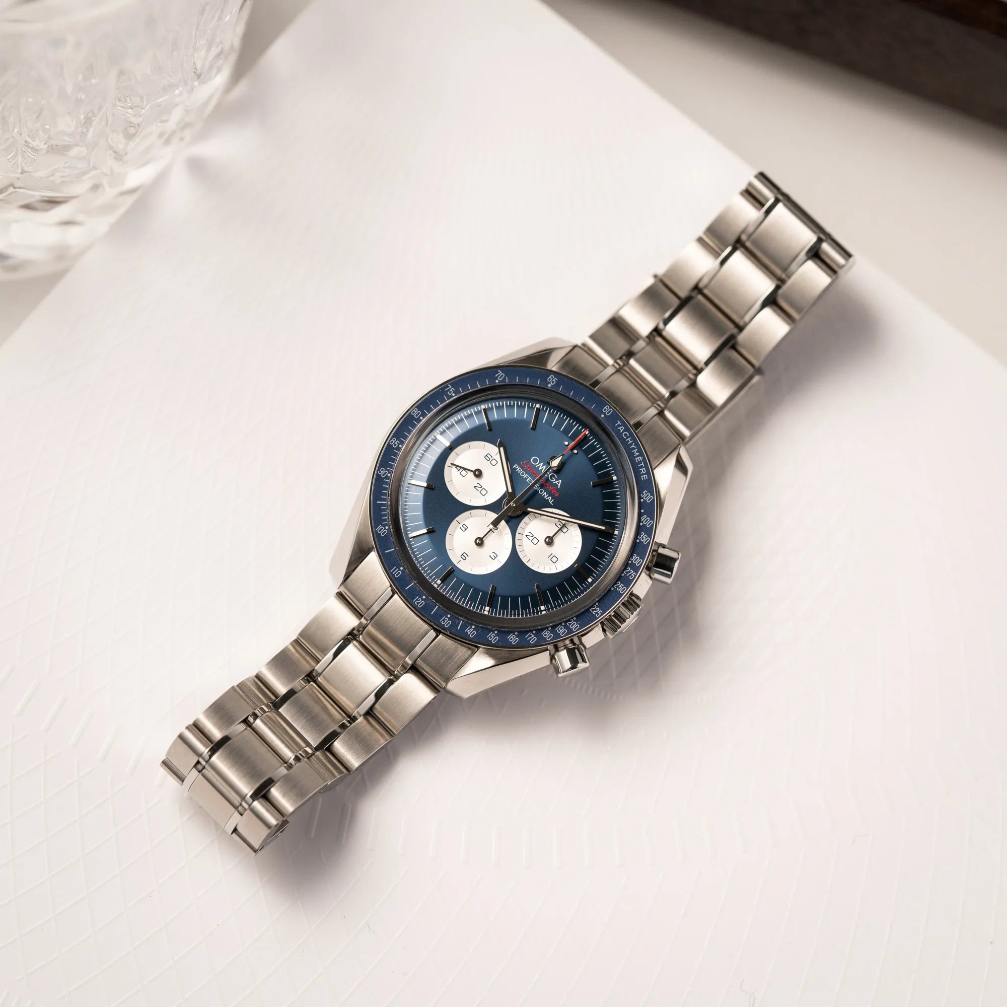 Omega Speedmaster Professional Moonwatch Tokyo Limited Edition mit blauem Zifferblatt und weißen Sub-Dials liegt flach auf einem Buch