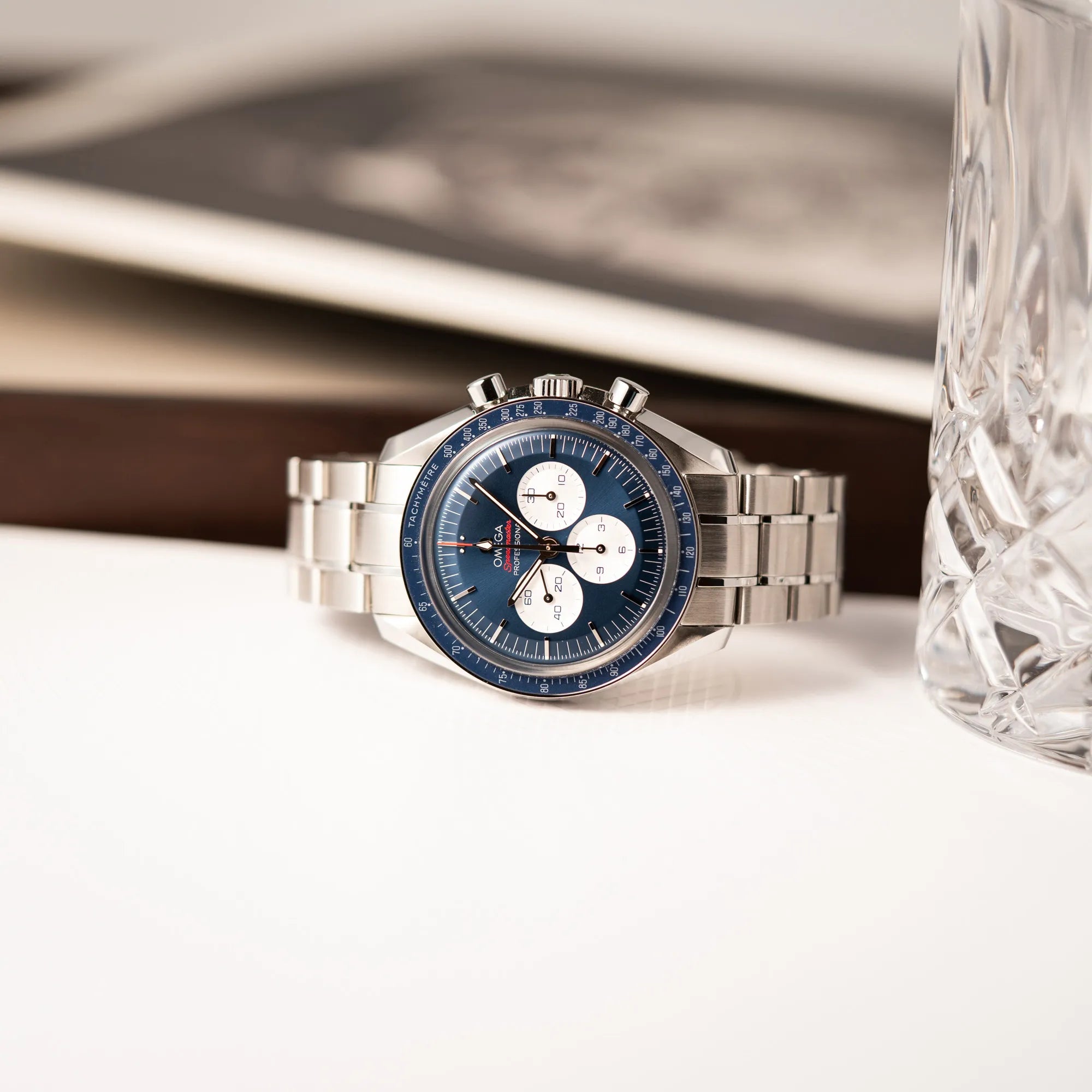 Produktfotografie der auf der seitlichen Gehäuseflanke liegenden Omega Speedmaster Professional Moonwatch Tokyo Limited Edition mit blauem Zifferblatt und weißen Sub-Dials