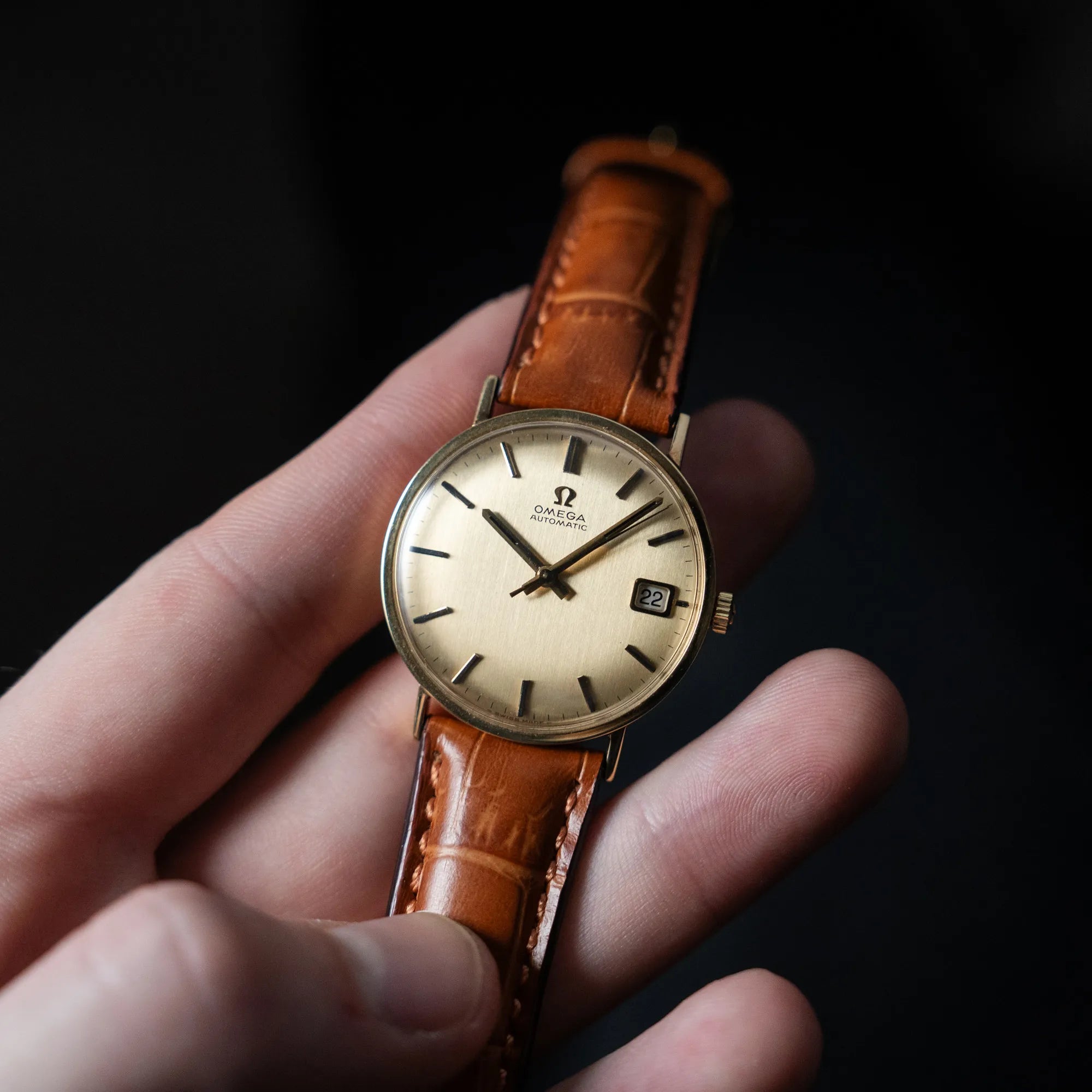 Mann hält die Omega Vintage Automatik Armbanduhr mit Gelbgold-Gehäuse in seiner Hand